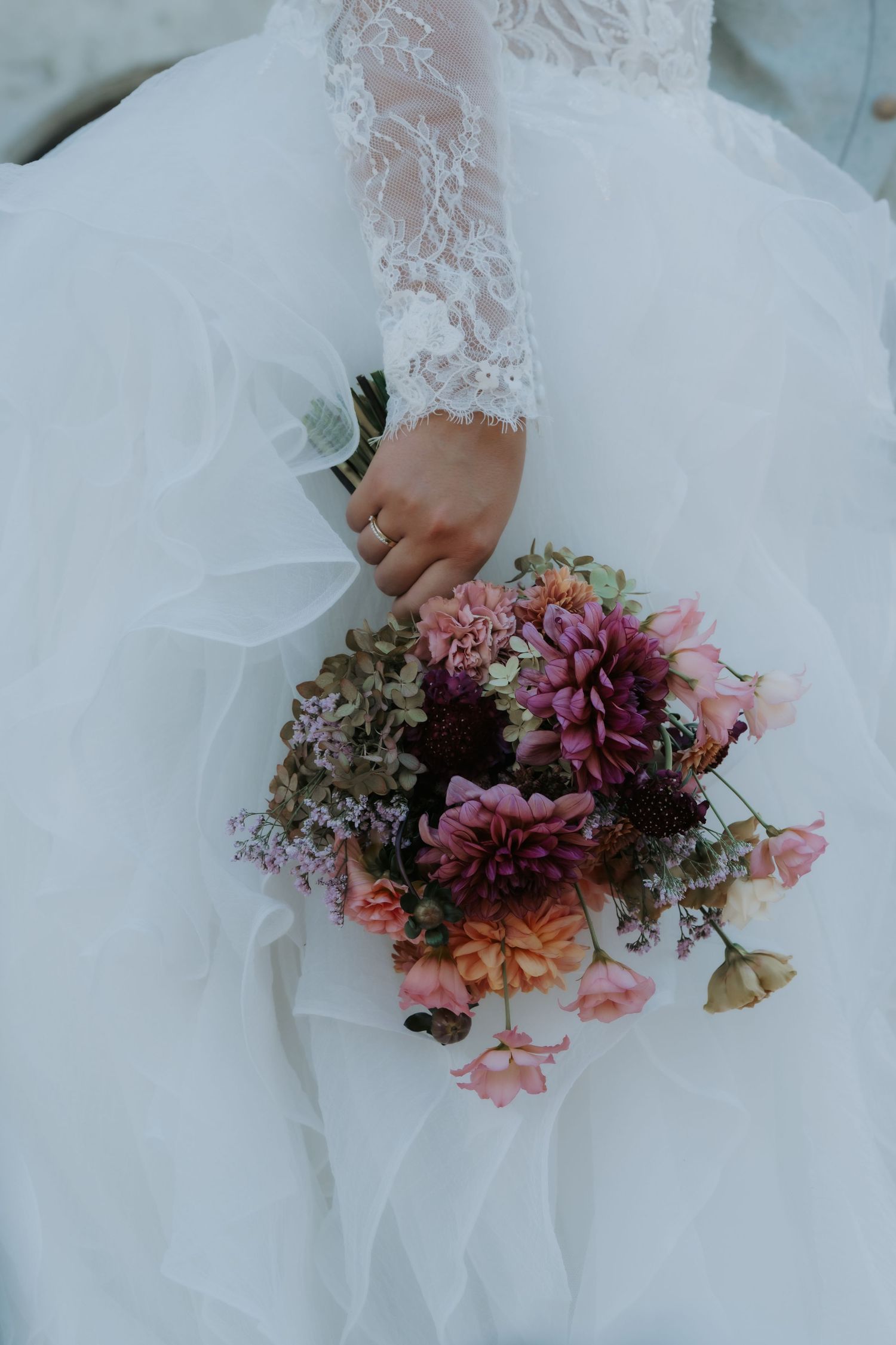 Bride in lace wedding gown holding a colorful bouquet of pink, purple, and orange flowers against her white tulle skirt.