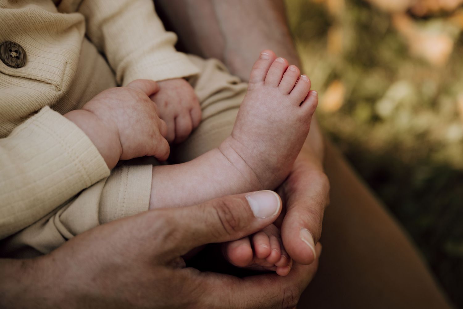 Close-up of a newborn baby's tiny feet cradled gently in adult hands, captured in warm natural light.