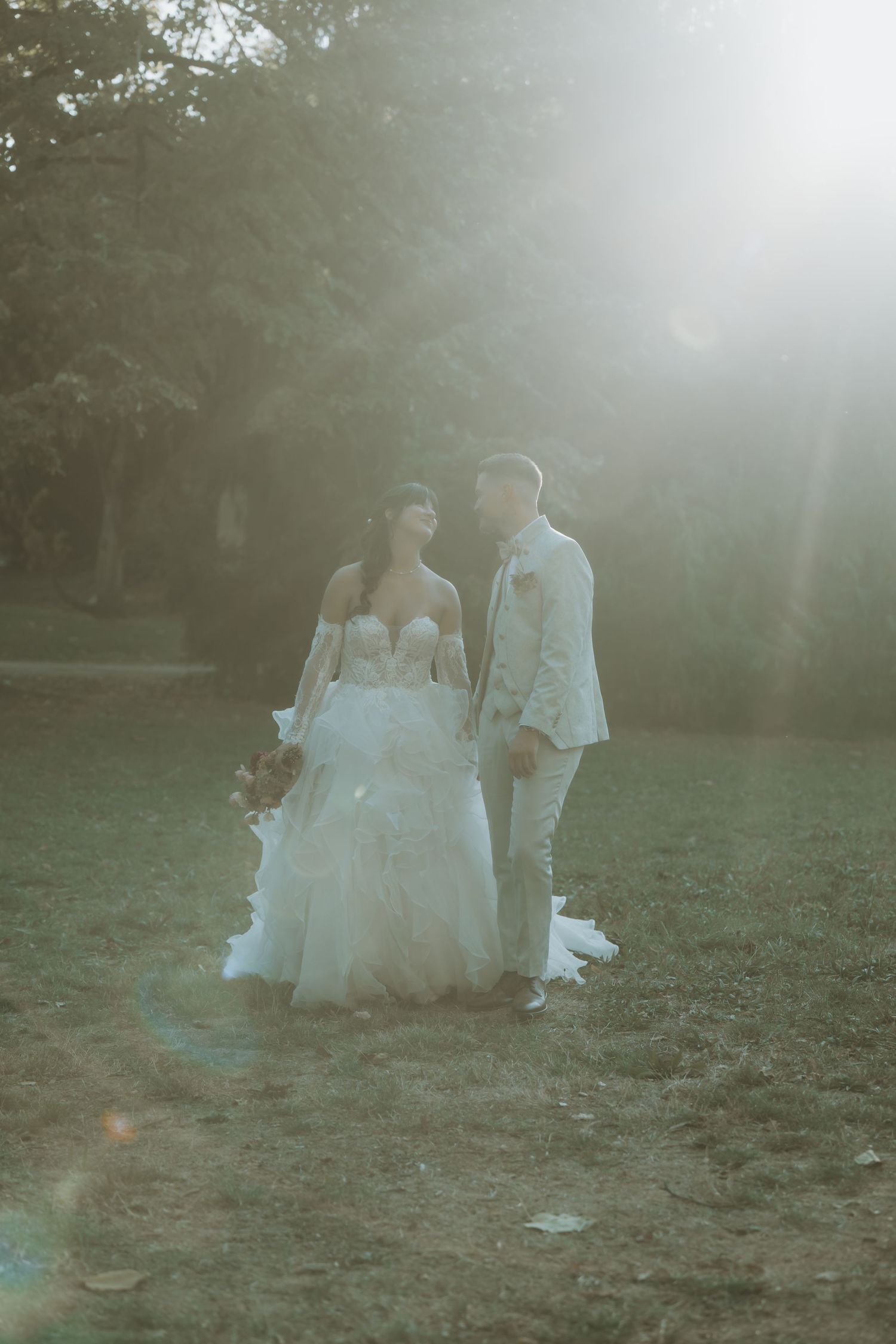 Bride and groom share a romantic moment outdoors, bathed in soft sunlight, with bride in elegant white tulle gown.