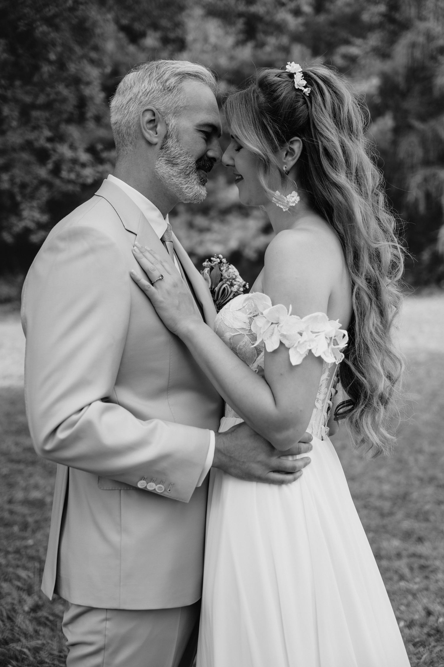 Black and white wedding photo of bride and groom embracing outdoors, foreheads touching romantically.