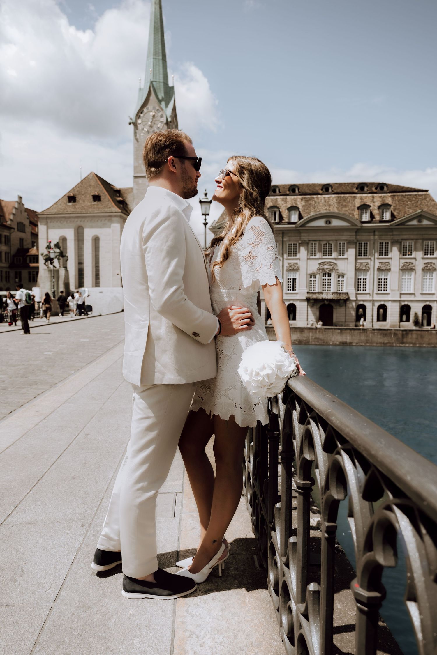Couple in wedding attire sharing a romantic moment on a bridge in Zurich, Switzerland, with historic architecture.