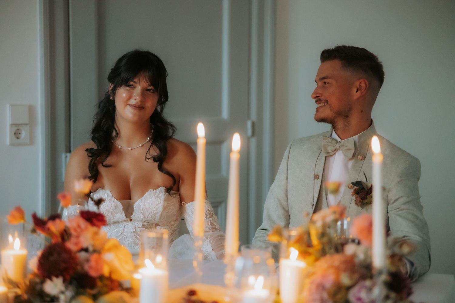 Bride and groom smiling at candlelit wedding reception table with floral centerpieces.