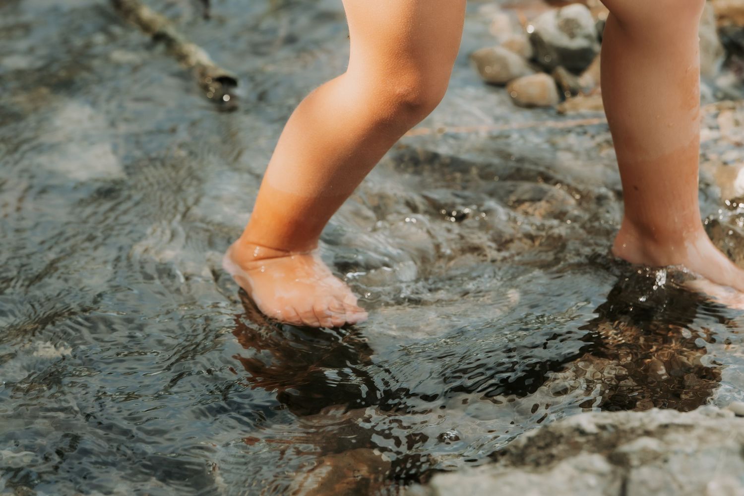 Child's bare feet splashing in shallow rocky stream water outdoors.