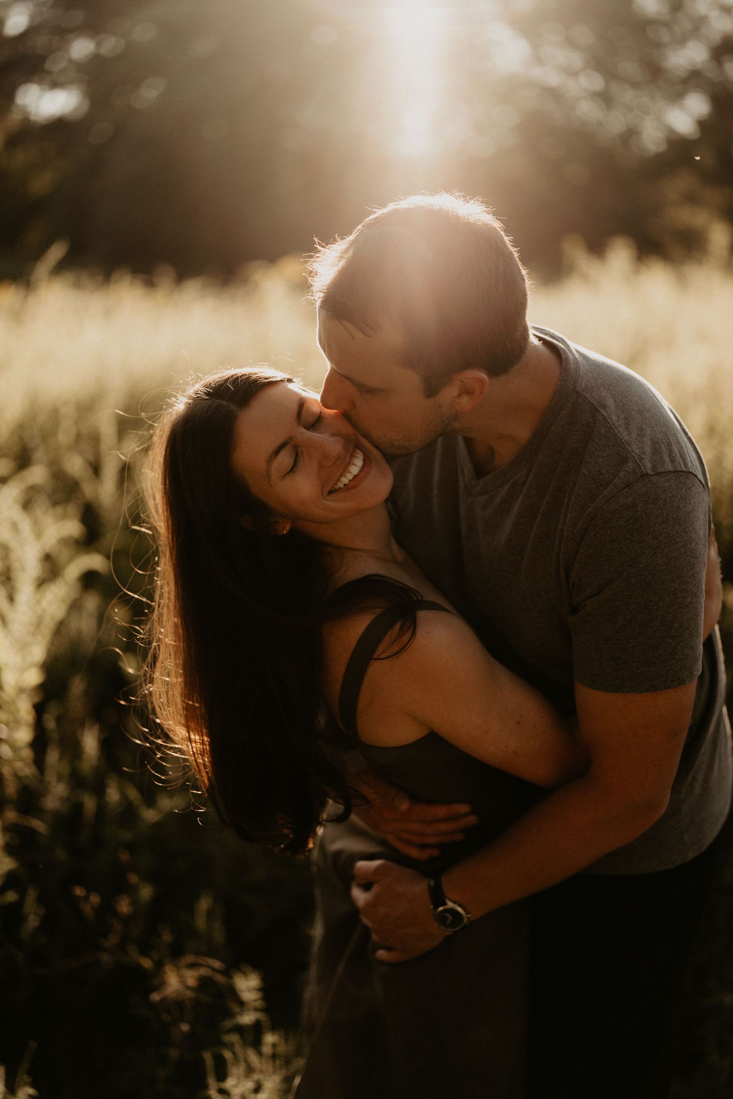 Couple embracing in golden sunlit field during sunset photoshoot.