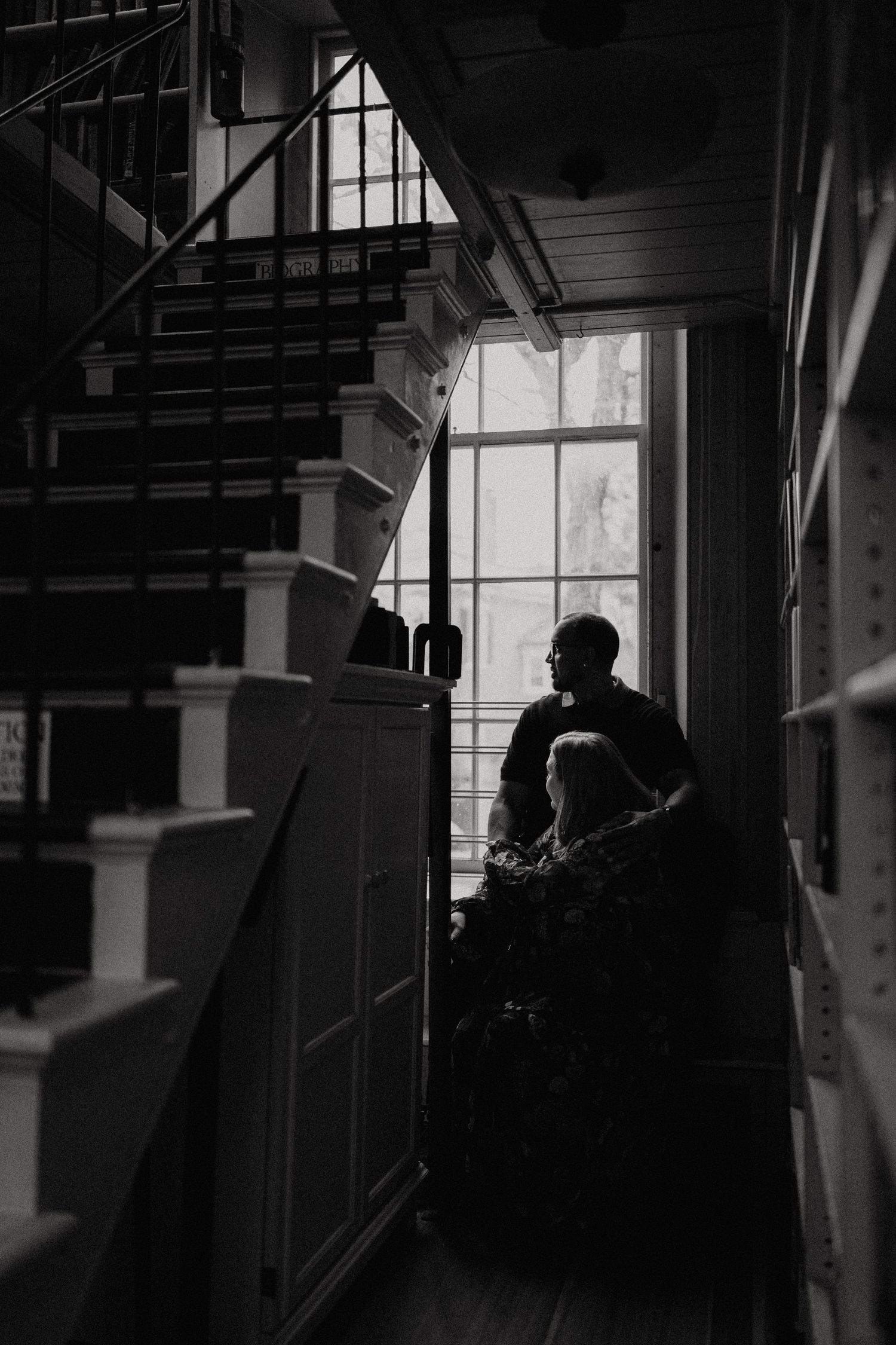 Silhouetted figures stand in a bright industrial space with large windows creating dramatic lighting and shadows.