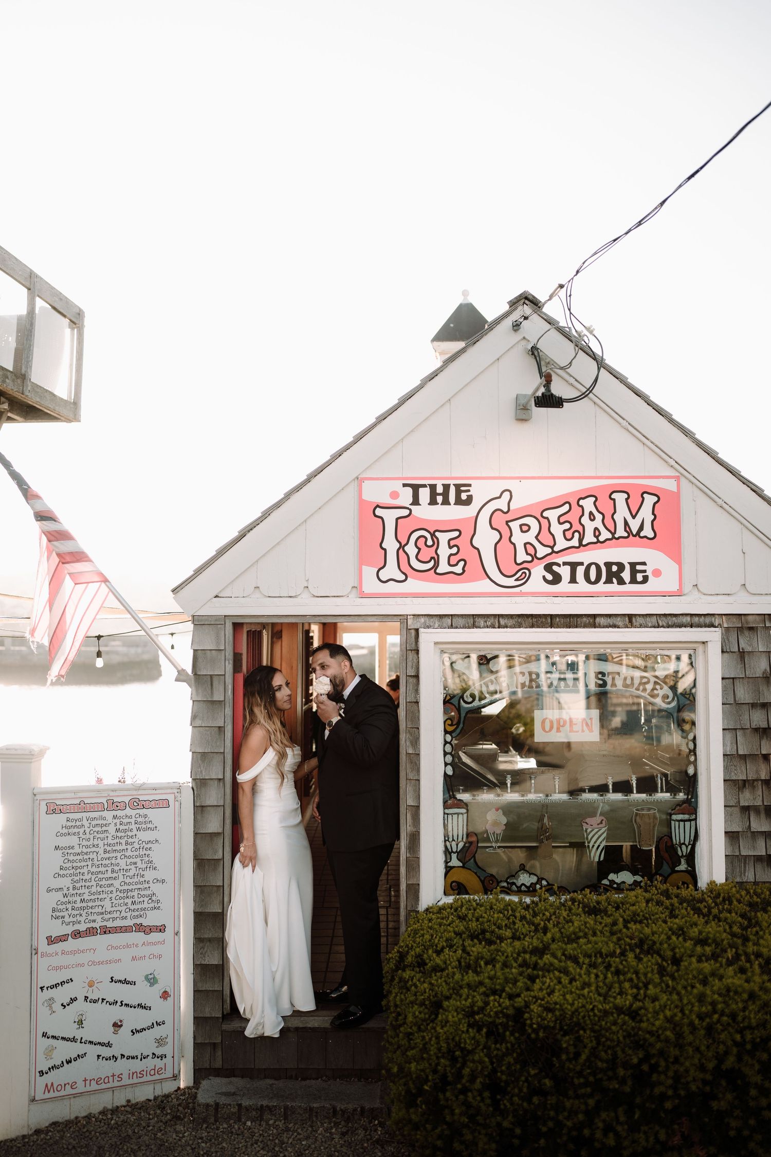 A couple stands in the doorway of a charming white ice cream store with a vintage red sign.