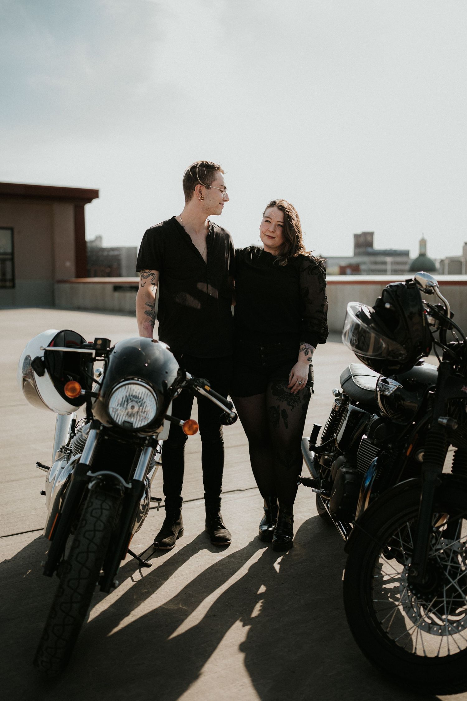 Couple sharing intimate moment beside parked motorcycles on urban rooftop.
