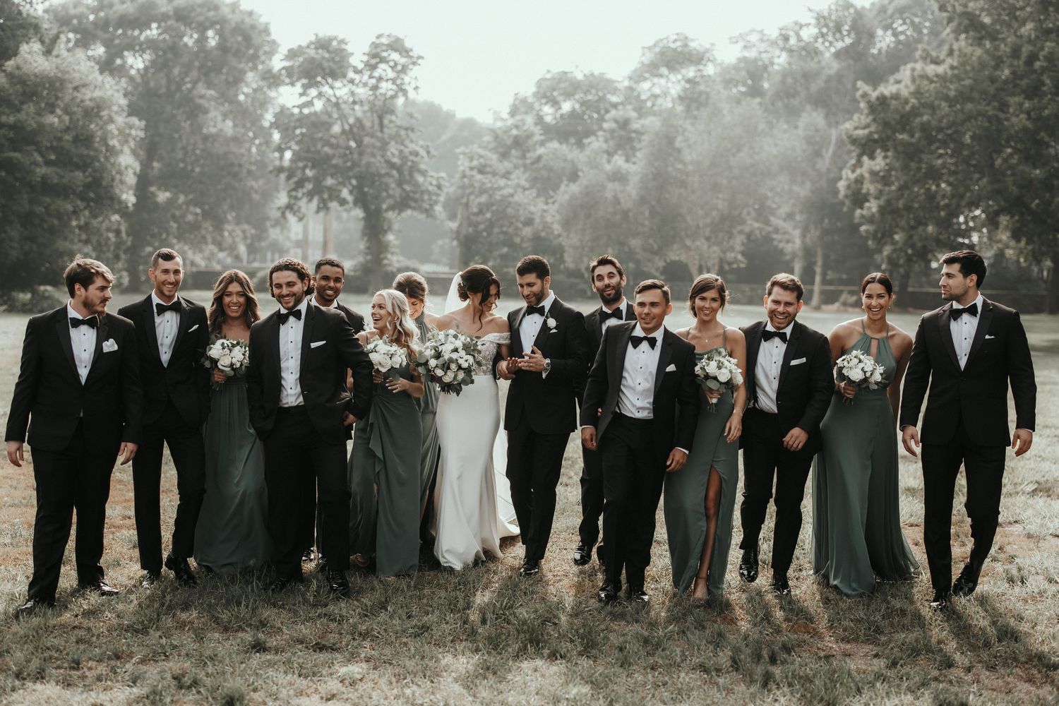 Wedding party in formal attire poses outdoors in a scenic natural setting.