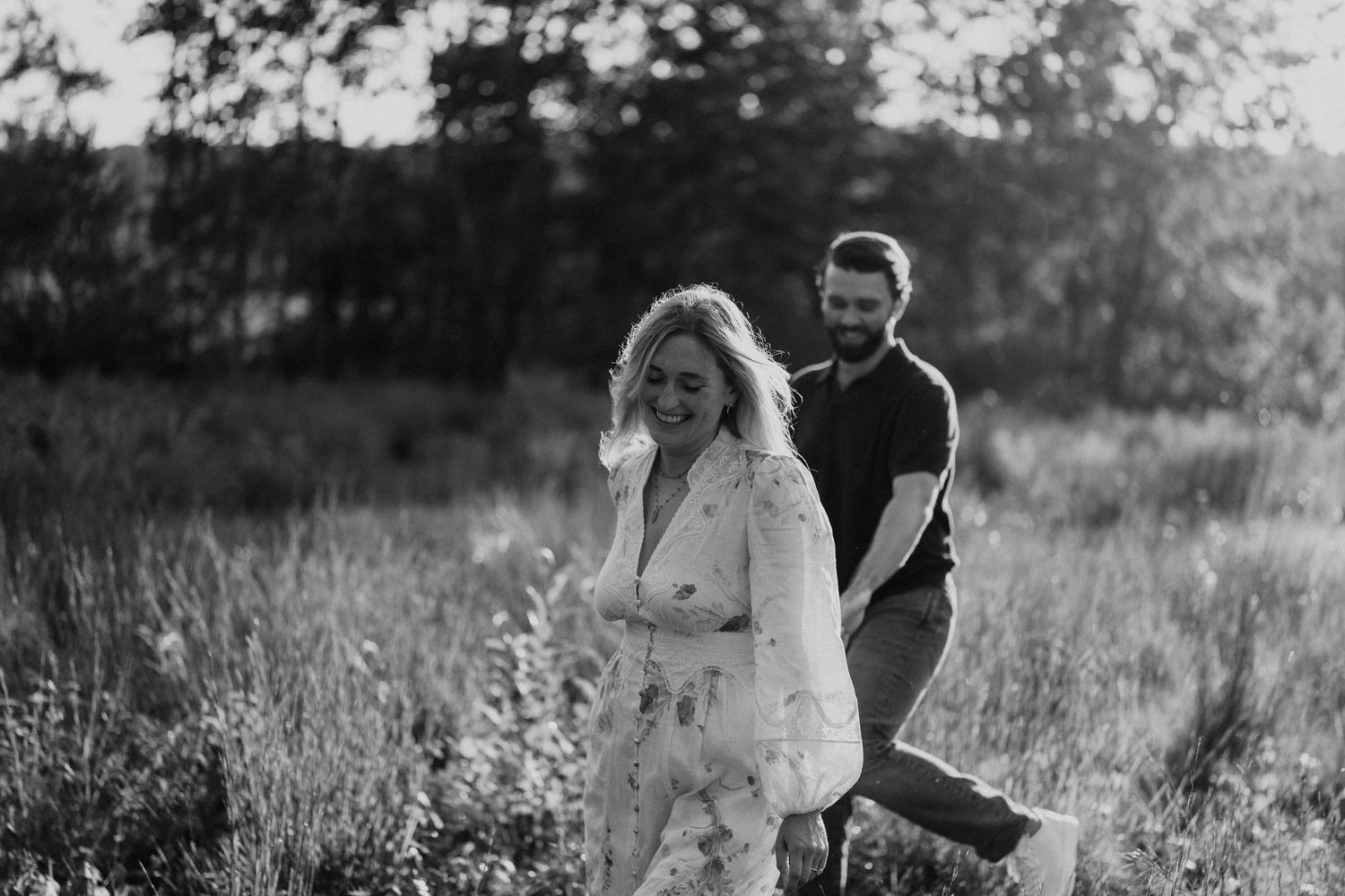 Couple walking hand in hand through a sunlit meadow with tall grass.