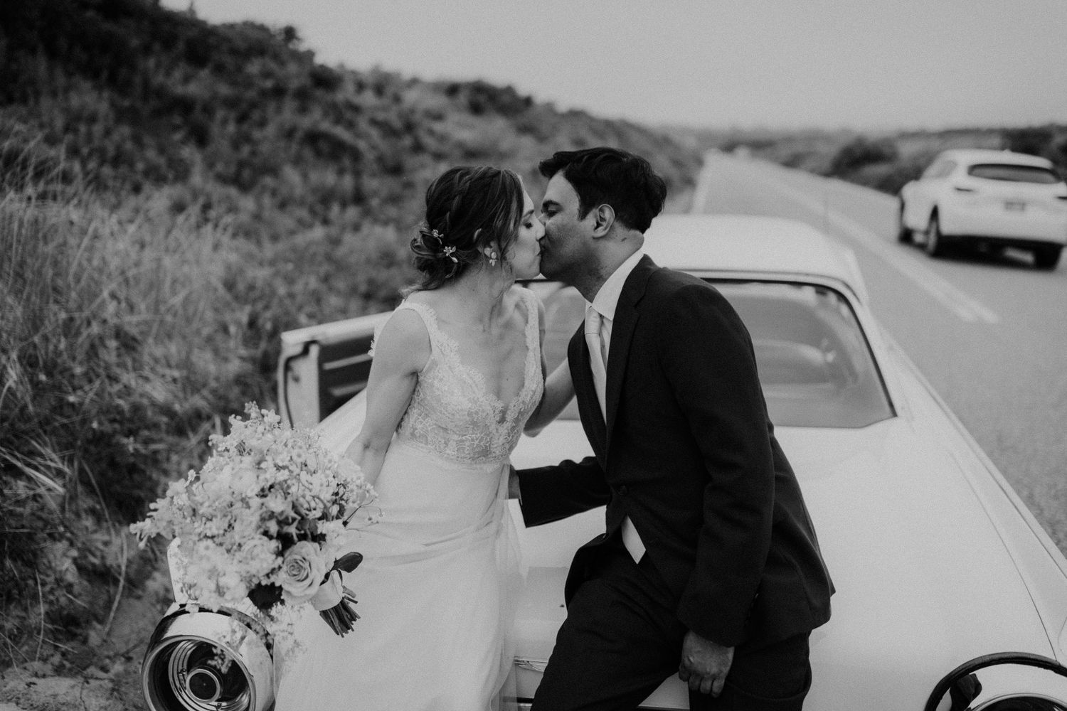 Black and white wedding photos showing romantic moments between a couple near vintage cars.