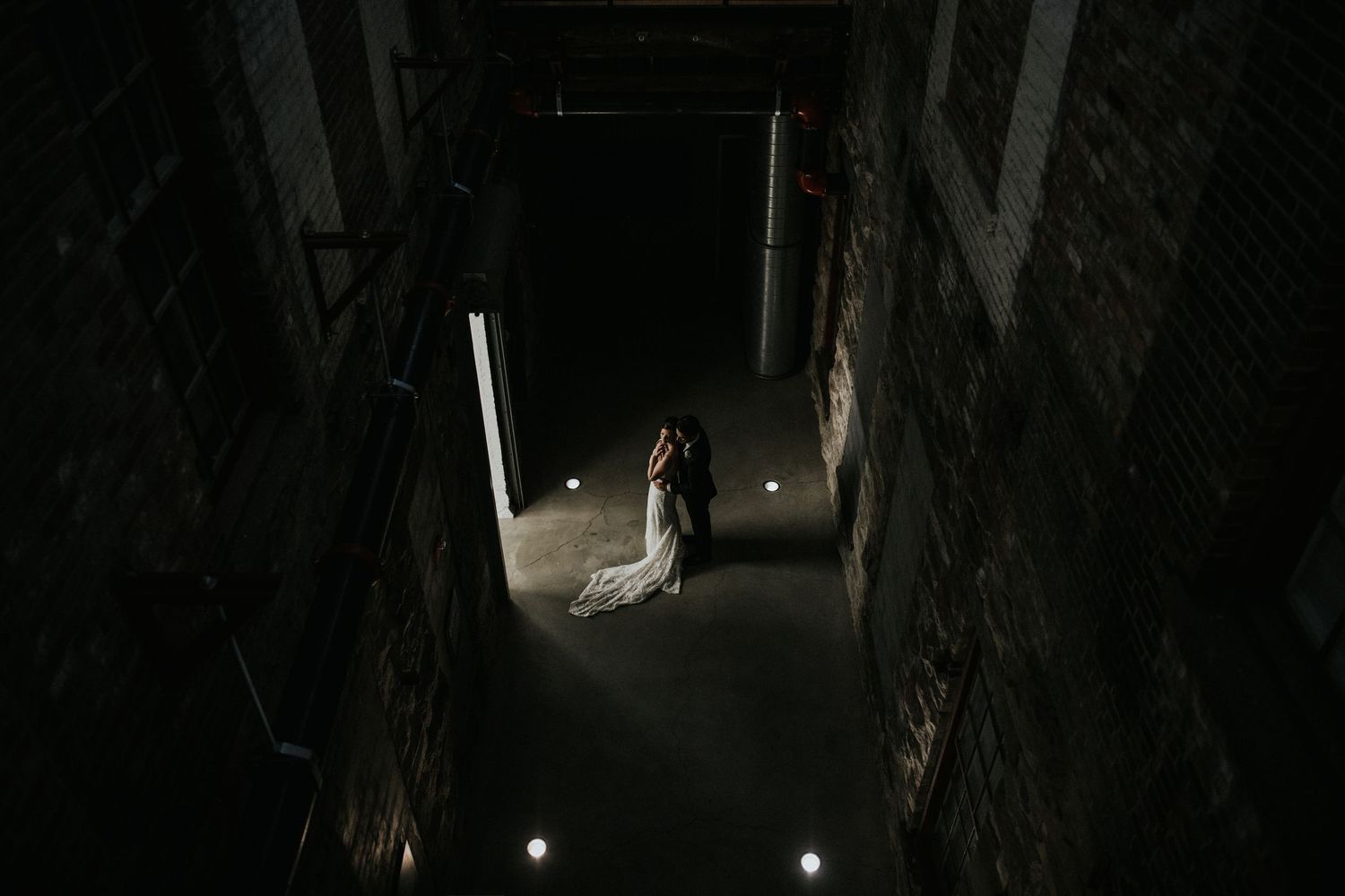 Dramatic wedding photo in dark industrial hallway with spotlight on bride.