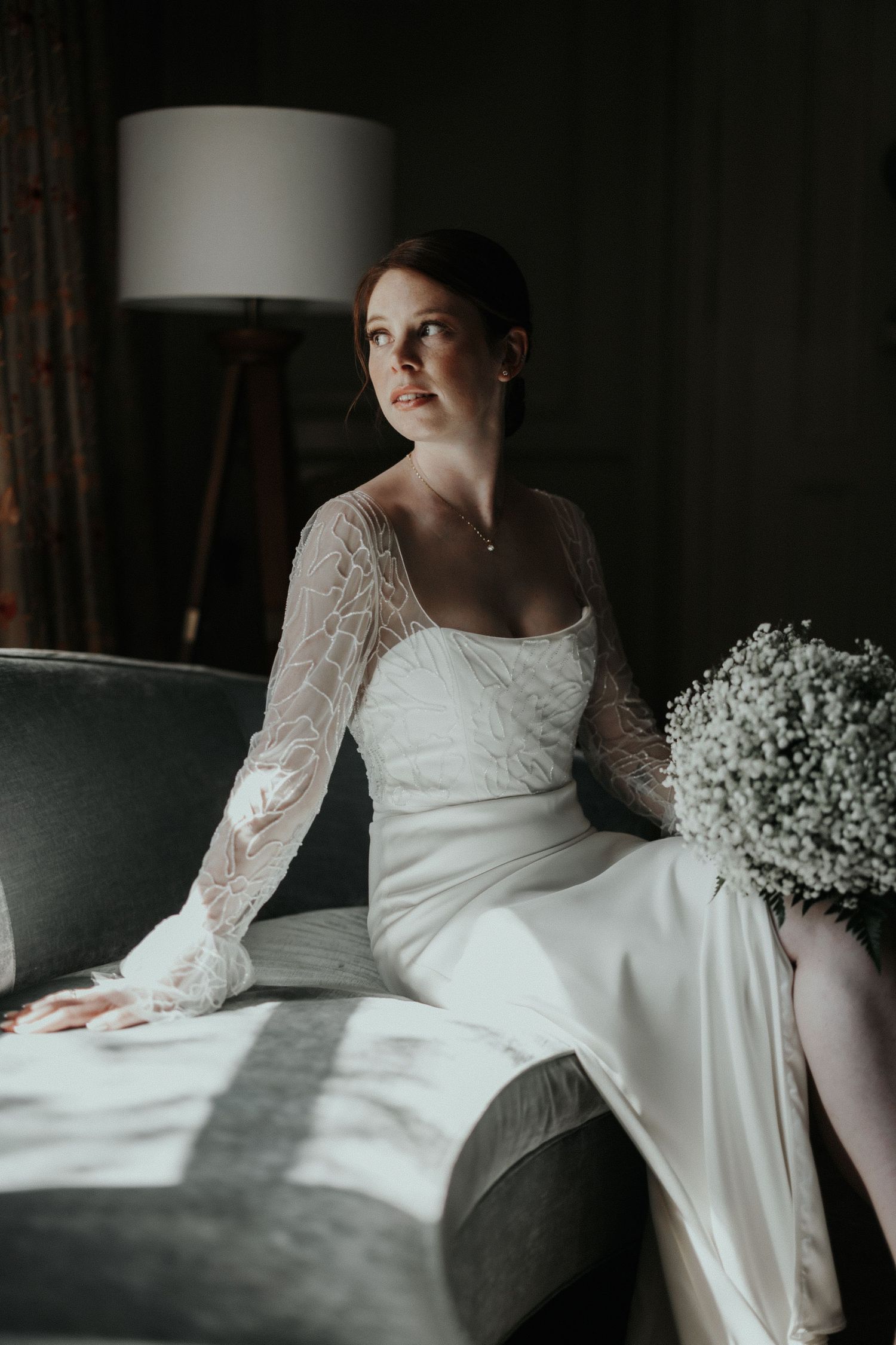 A white lace wedding dress with long sleeves photographed in moody lighting with baby's breath flowers.
