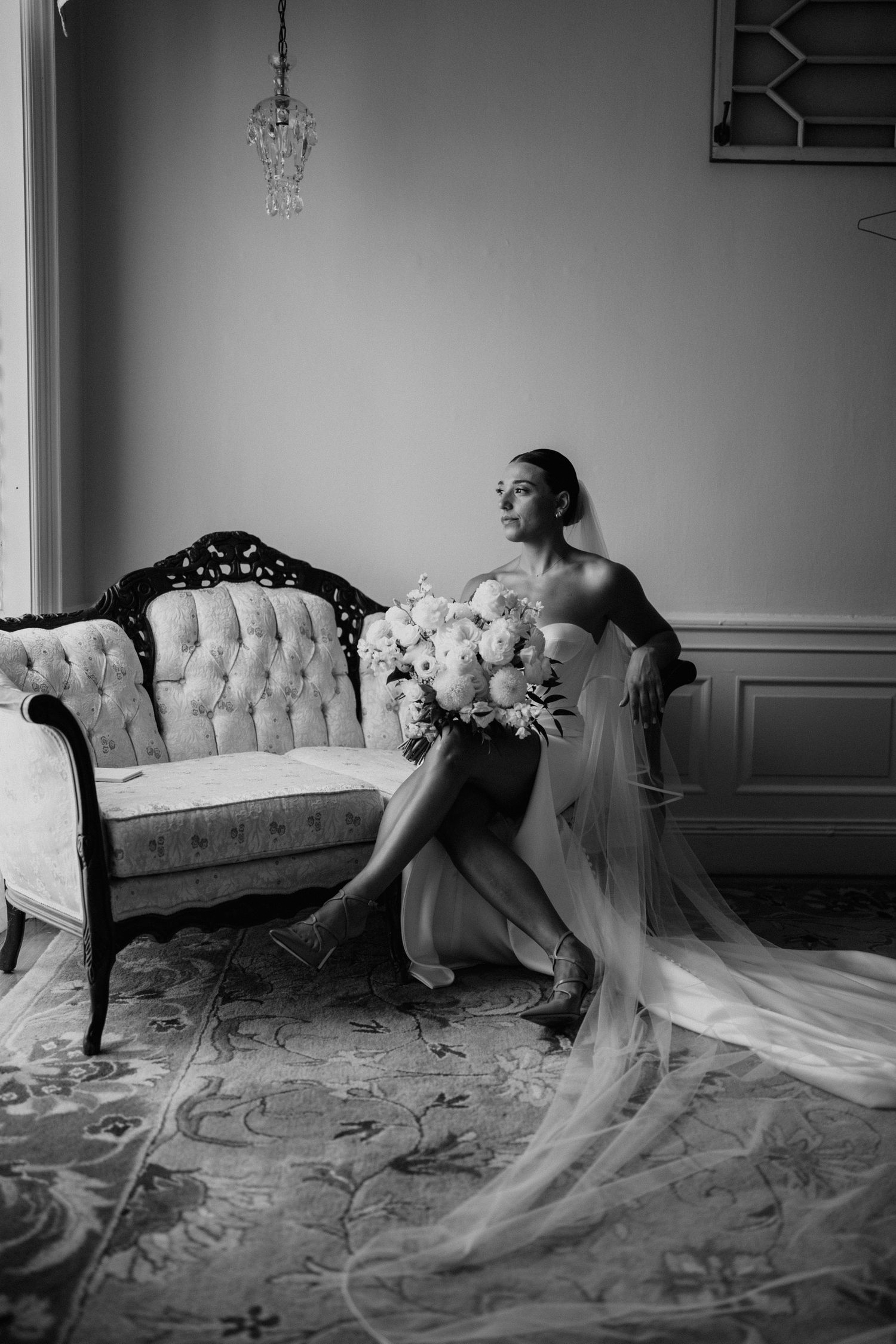 Artistic black and white series showing a bride posing dramatically with a flowing veil on a vintage sofa.