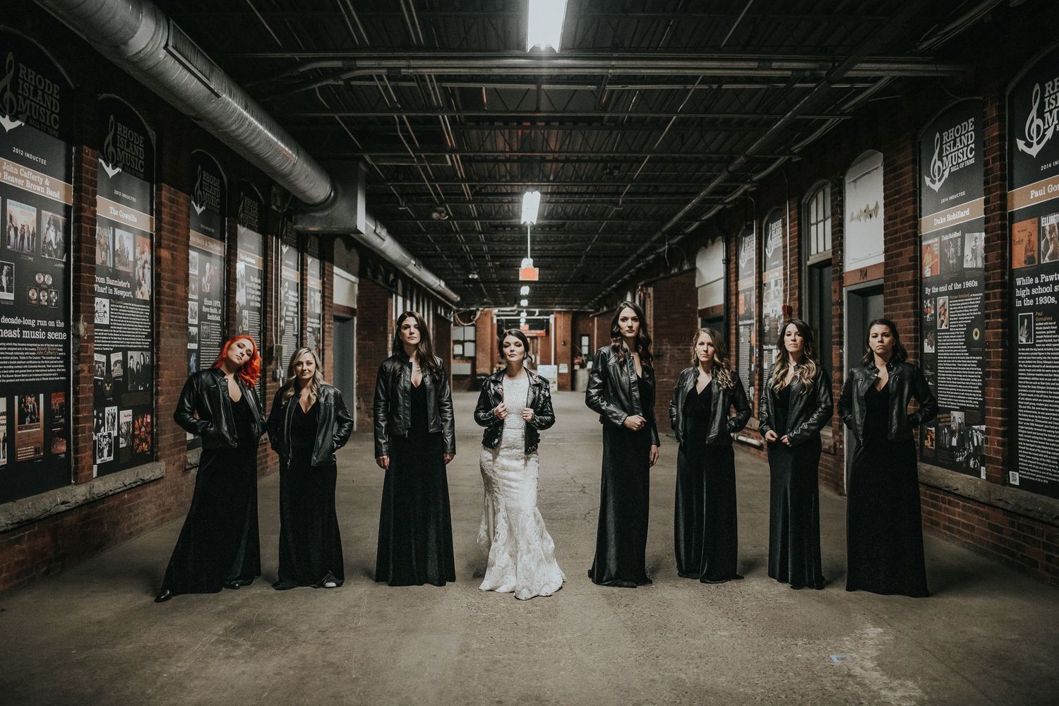 Wedding party lines industrial hallway in contrast of formal attire against urban setting.