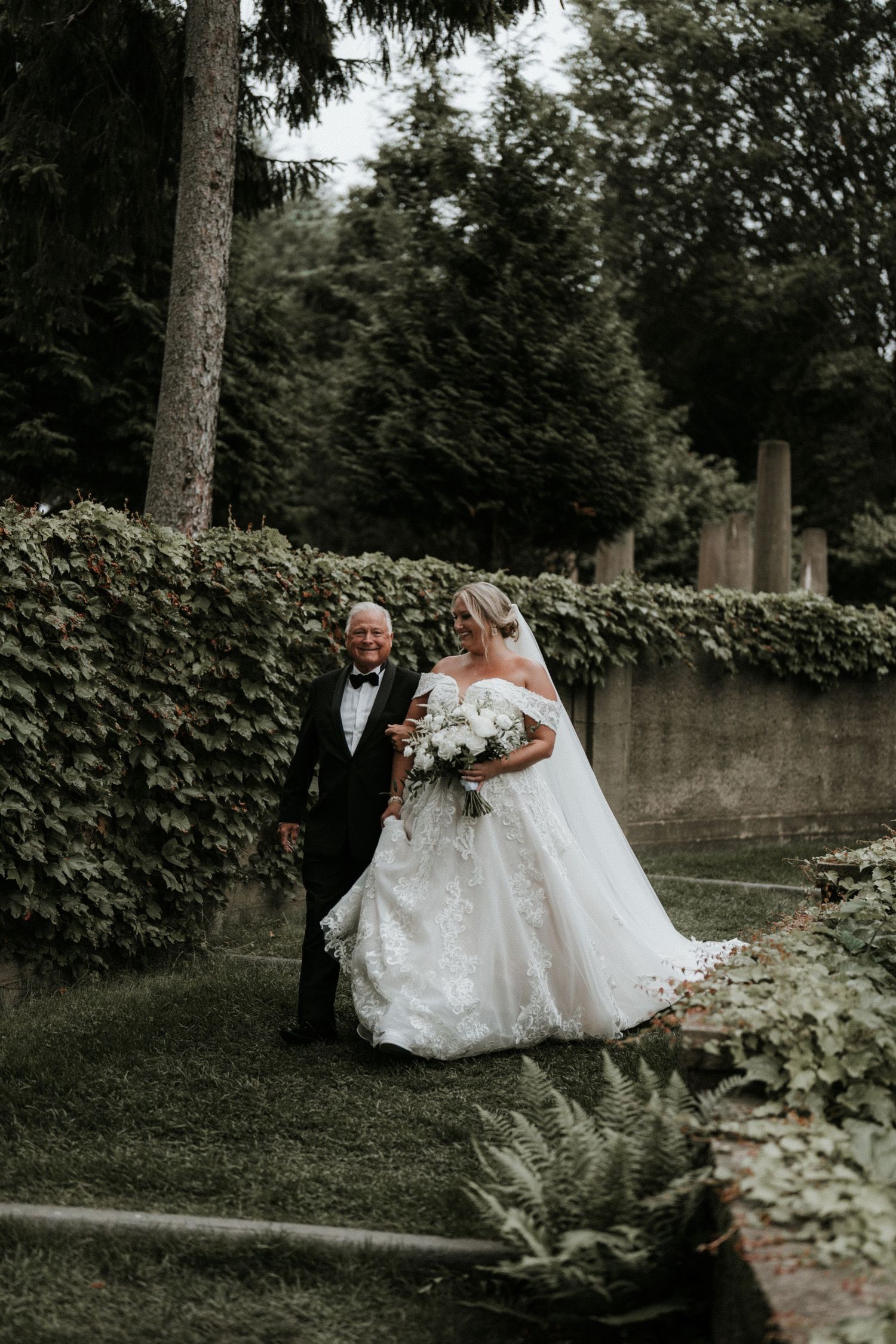 Wedding couple poses in garden setting with ivy covered walls and natural greenery.