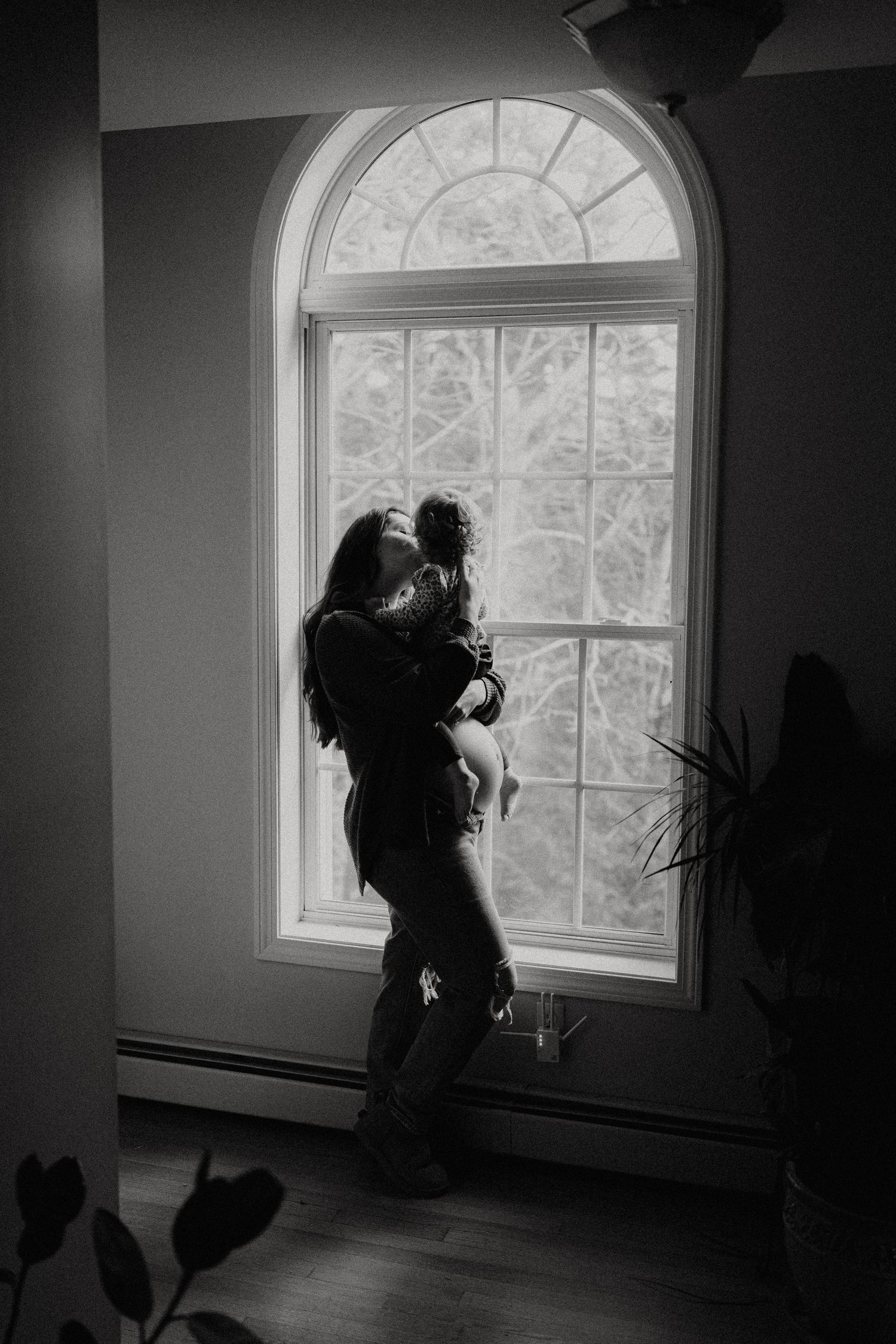 Silhouetted figure stands by arched window in dramatic black and white interior series.
