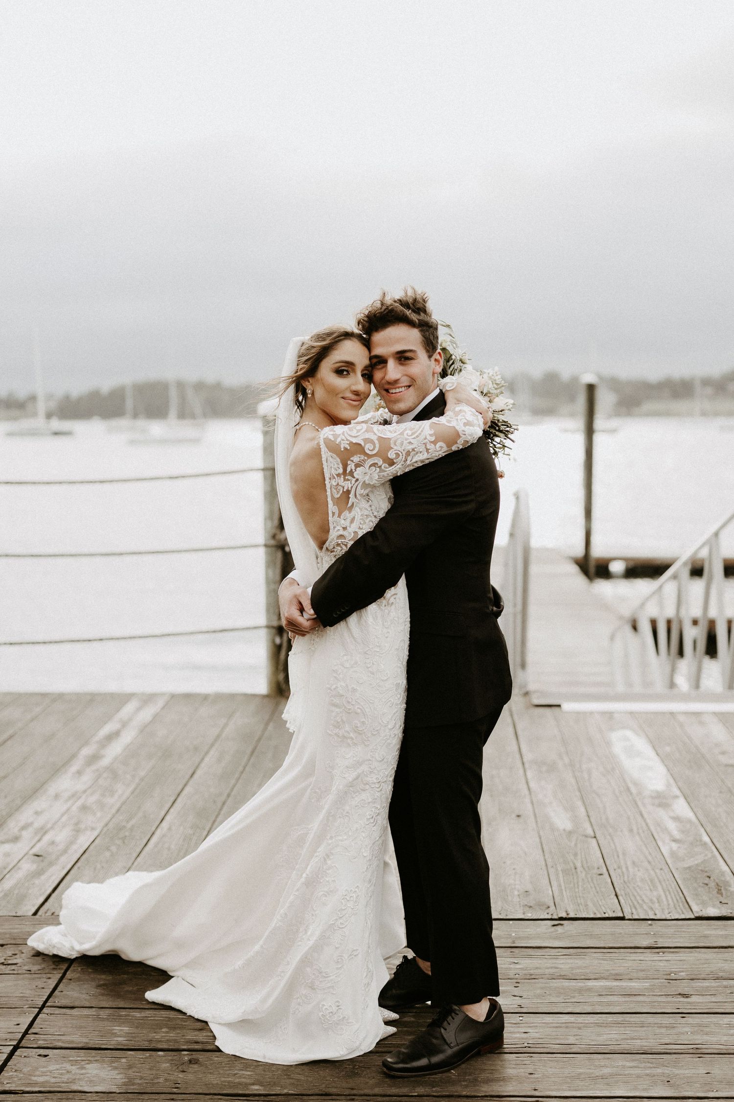 Romantic black and white portrait of newlyweds embracing on wooden dock.
