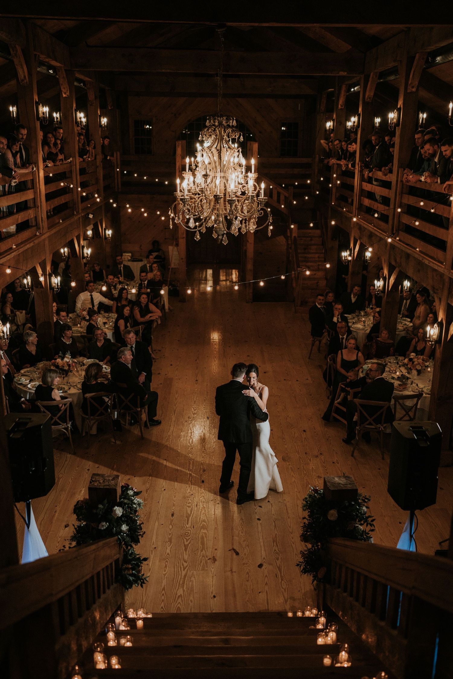 A dimly lit ballroom wedding reception with chandeliers and candlelight creating a romantic atmosphere.