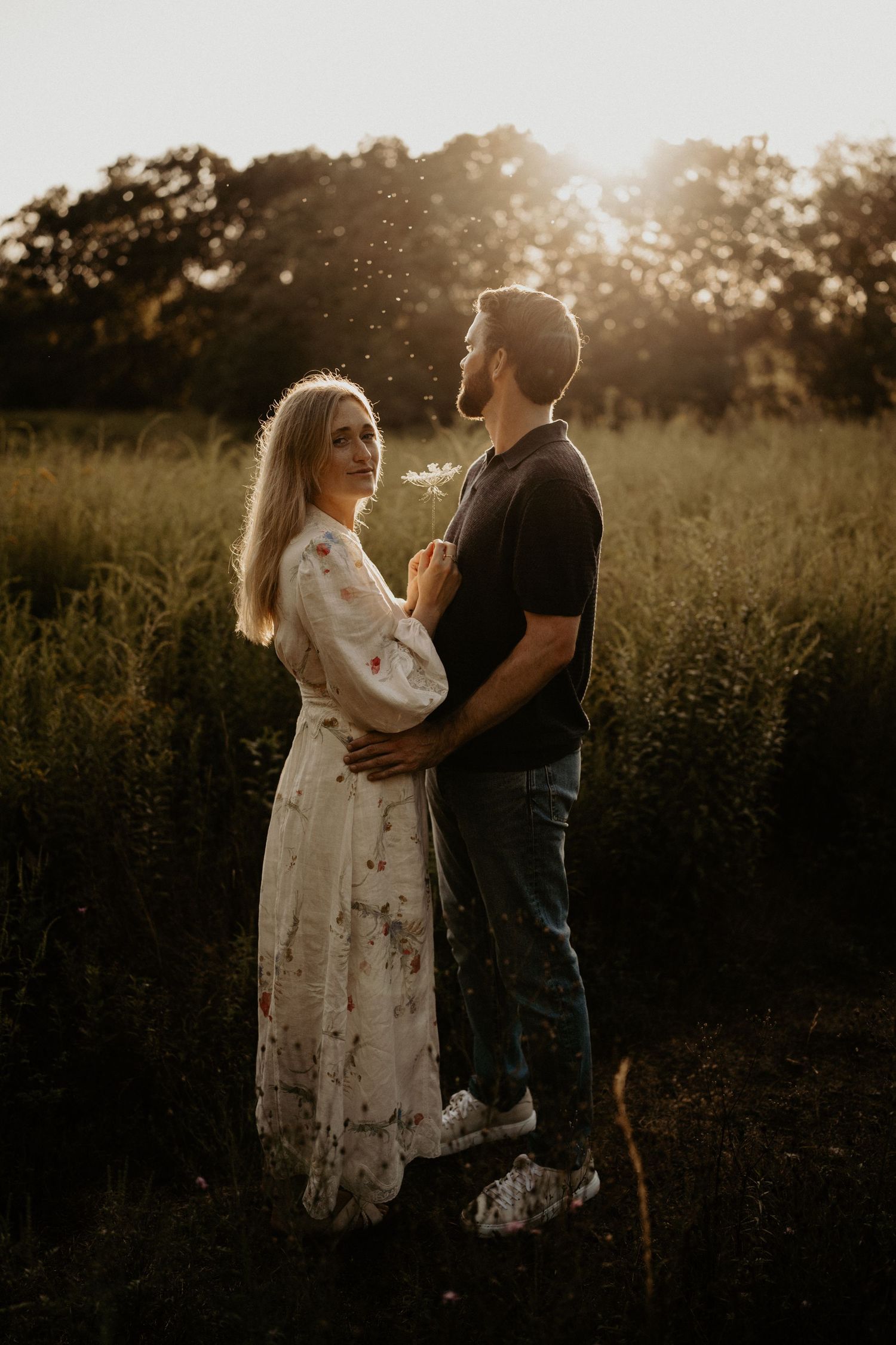 A couple shares an intimate moment in a sunlit field at golden hour.