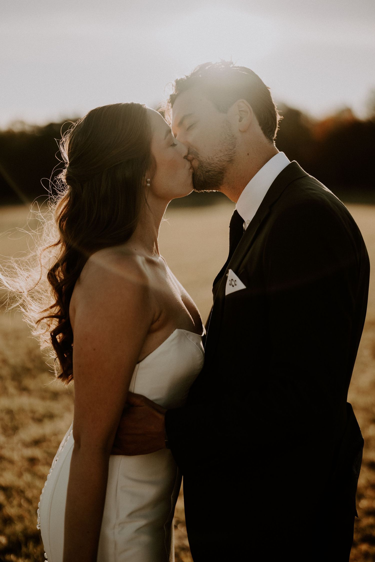 A romantic wedding couple shares an intimate moment at sunset in a golden field.