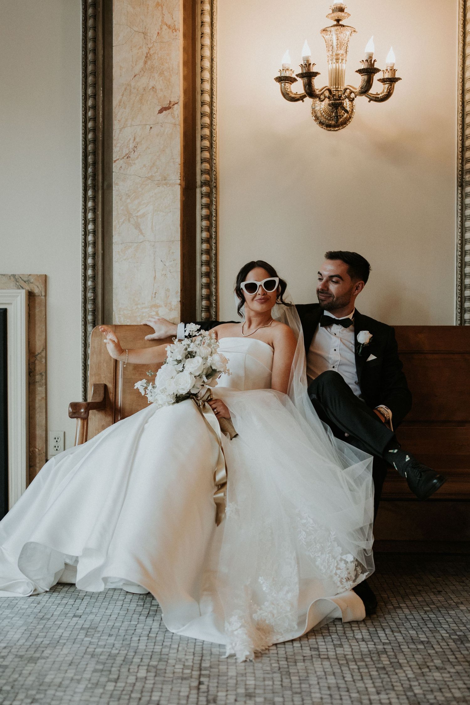 Stylish newlyweds pose in vintage venue with elegant chandelier.