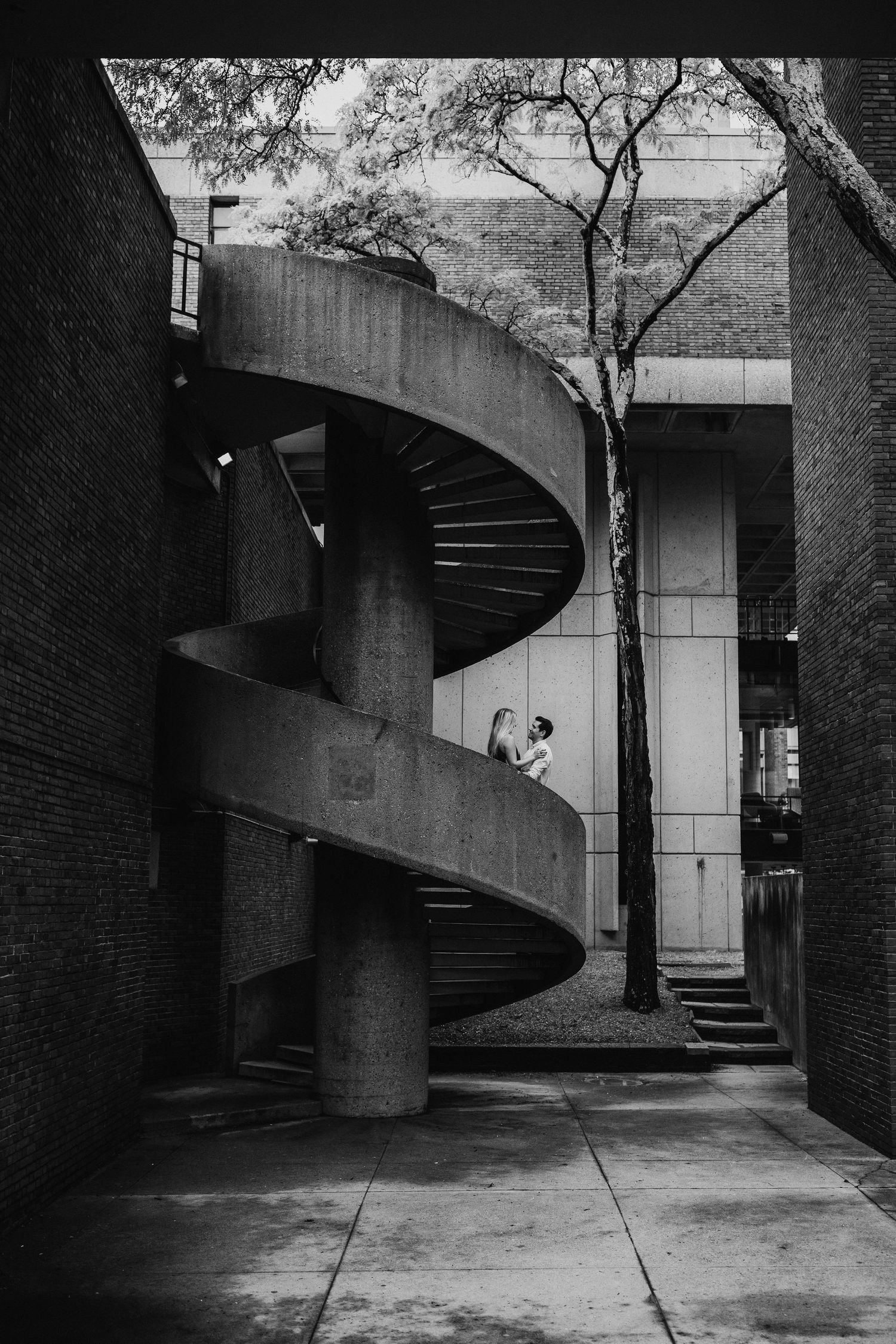 A dramatic black and white architectural view of a spiral staircase in an urban setting.