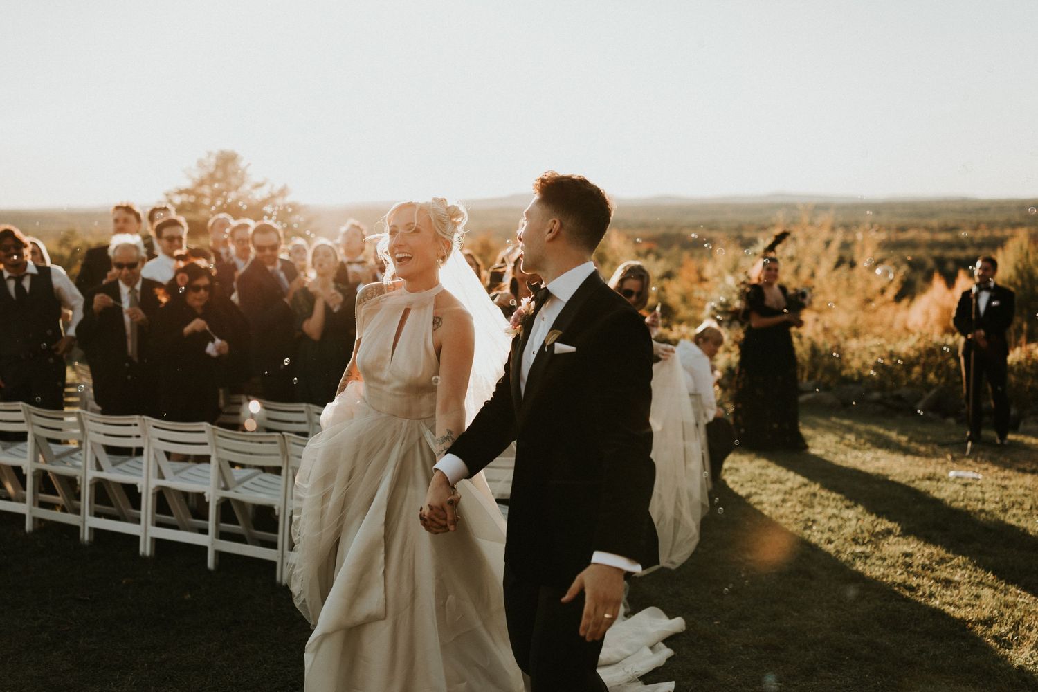 Couple embraces during golden hour at outdoor wedding ceremony with scenic mountain views in background.