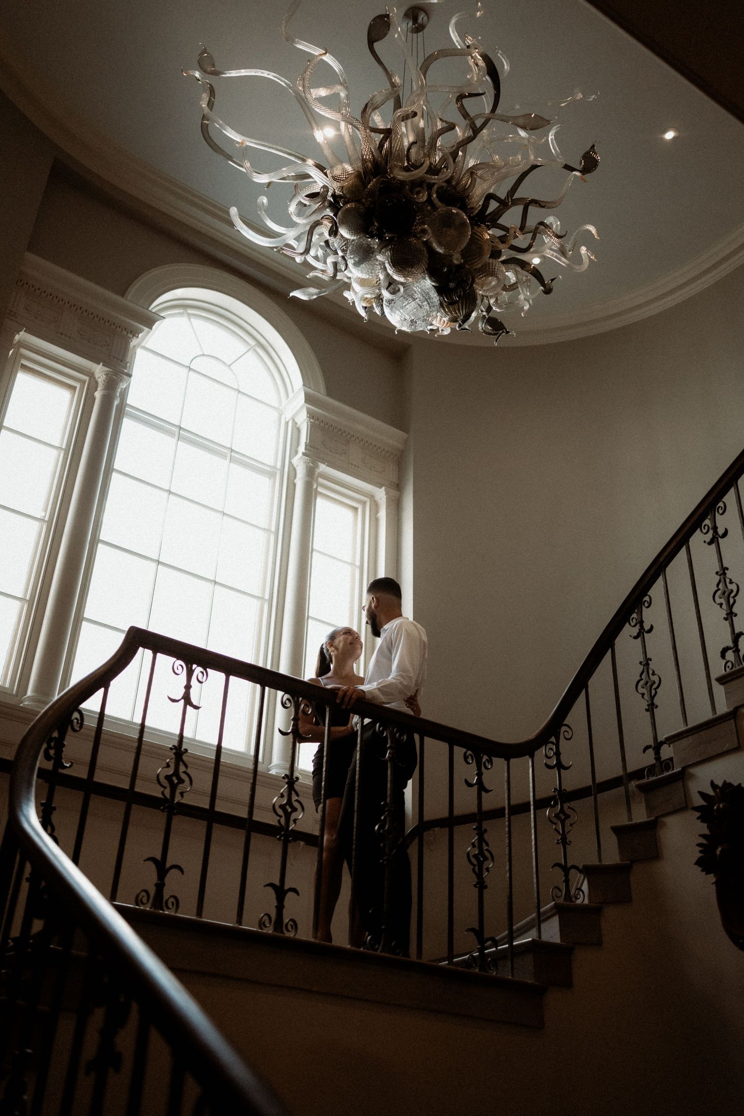 Elegant staircase scene with ornate railings and dramatic window lighting.
