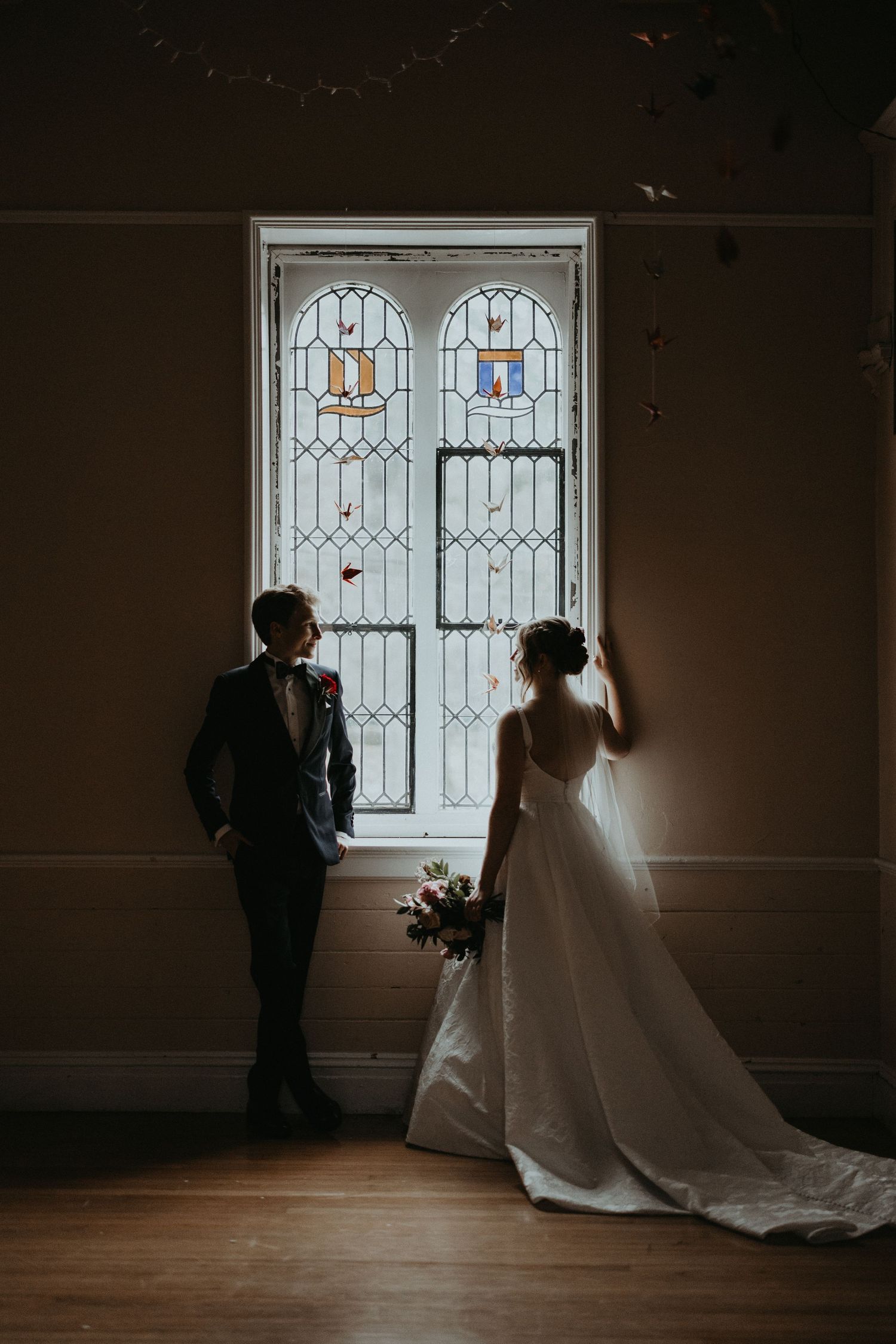 A couple in wedding attire stands silhouetted against a beautiful stained glass window.
