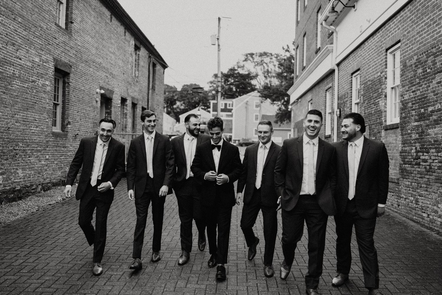 A group of formally dressed people walk together down a brick-paved street.