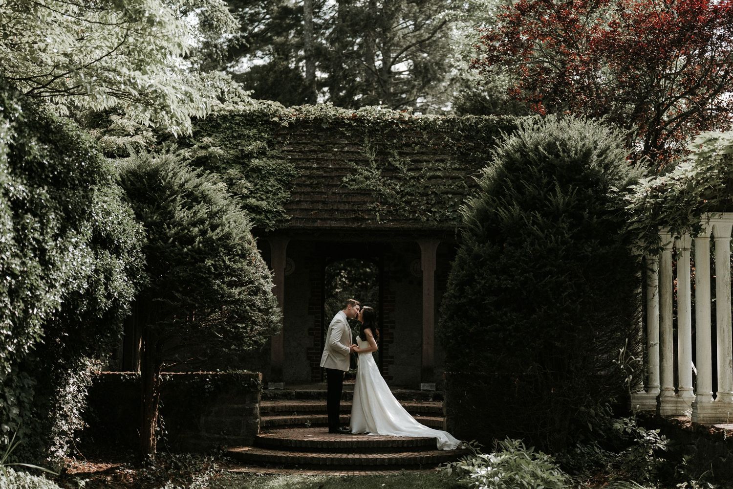 A wedding ceremony setup in a lush garden with white chairs and floral arrangements.