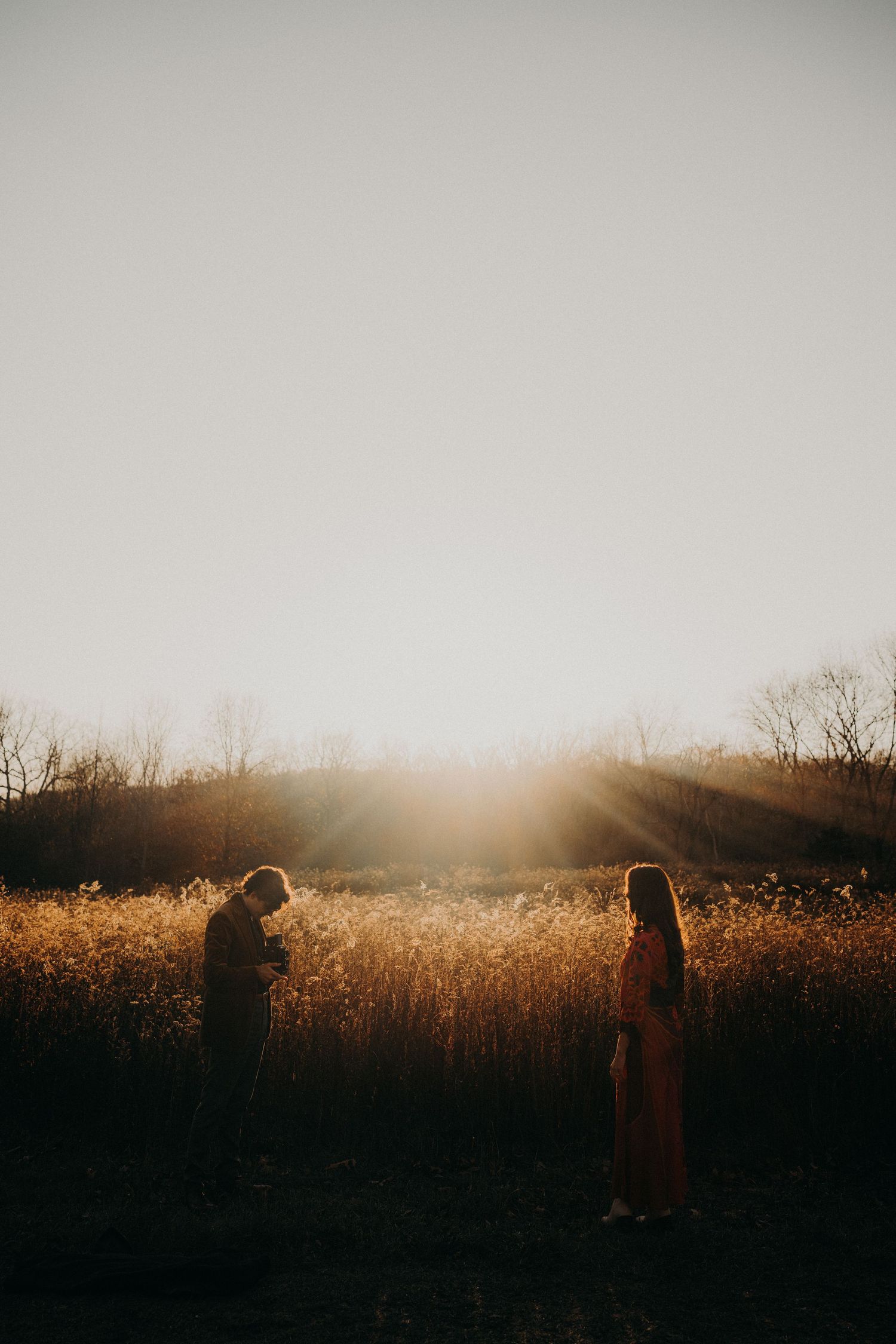 Two silhouettes stand together in a golden field during sunset.