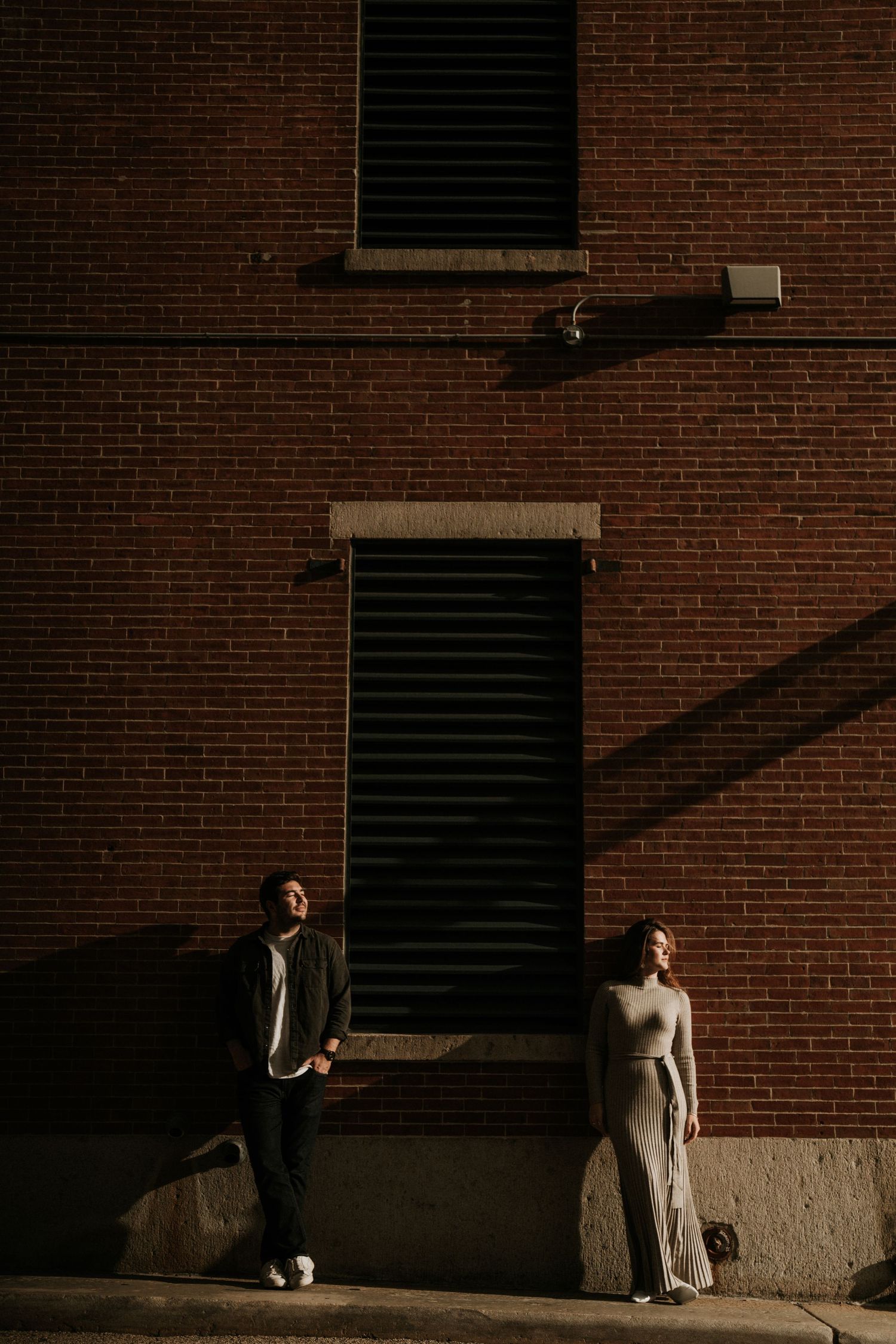 Artistic wedding photo of a couple posed against a brick wall with dramatic shadows.