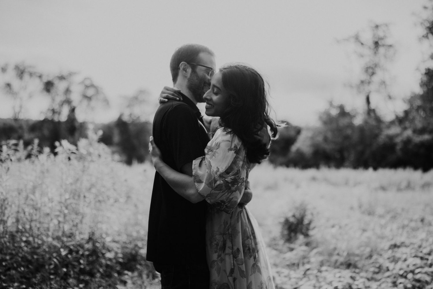 A couple embraces in a sunlit field during a black and white photoshoot.