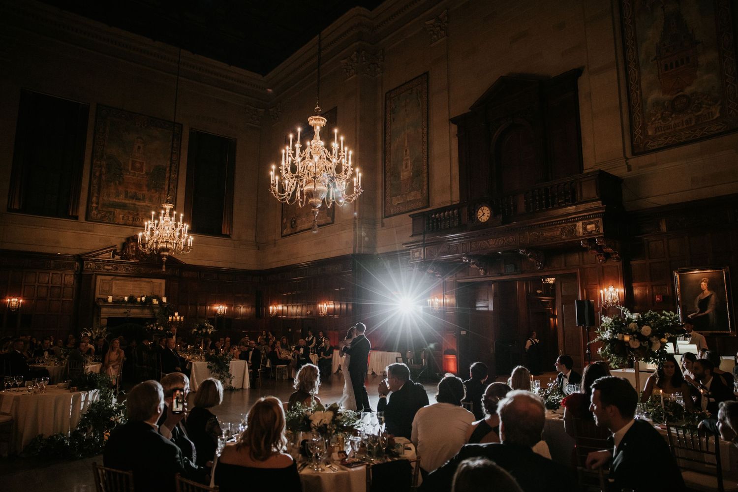 Dark reception hall with chandeliers and silhouettes of guests creating an atmospheric ambiance.
