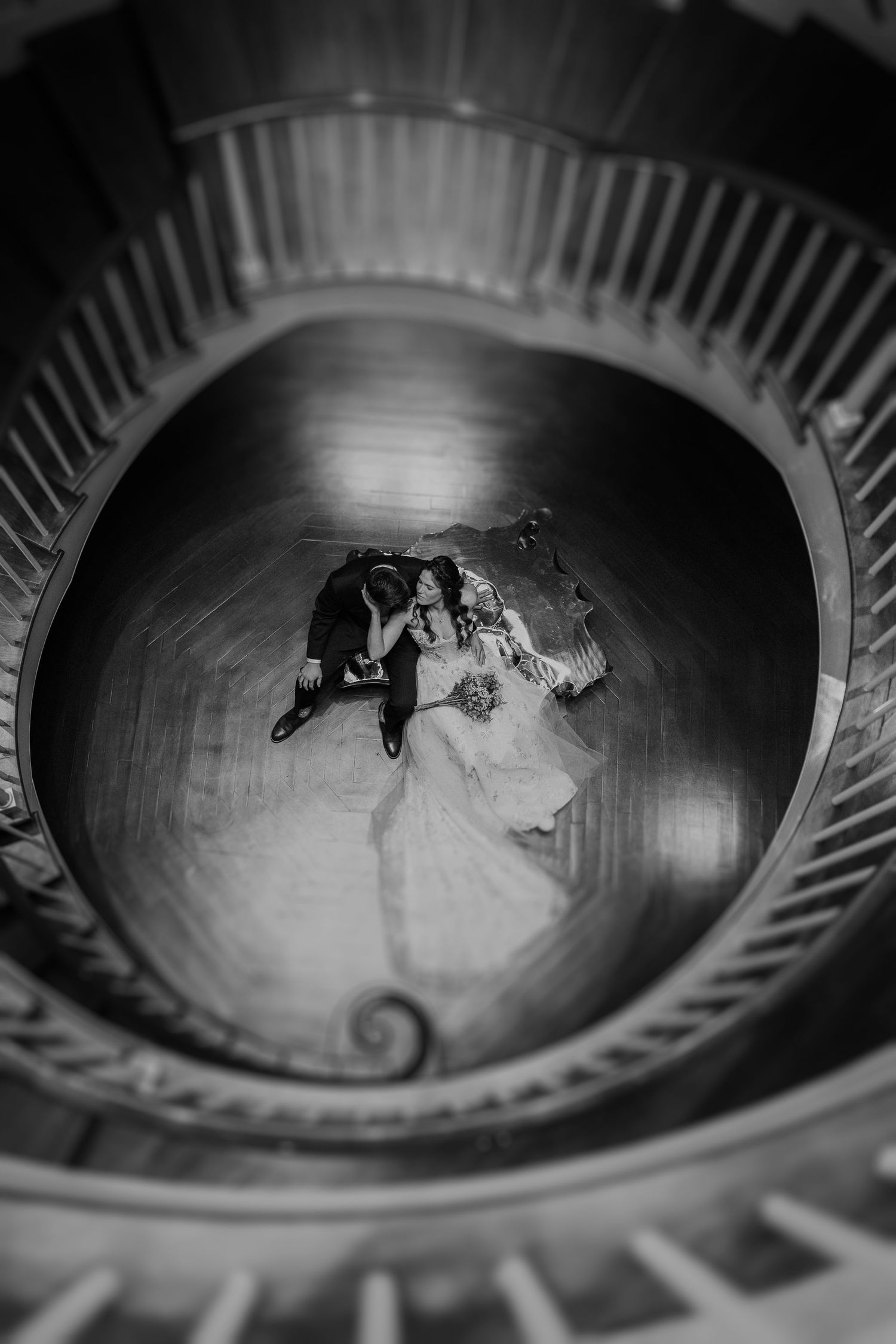 Overhead spiral staircase view of a couple in formal attire in black and white.