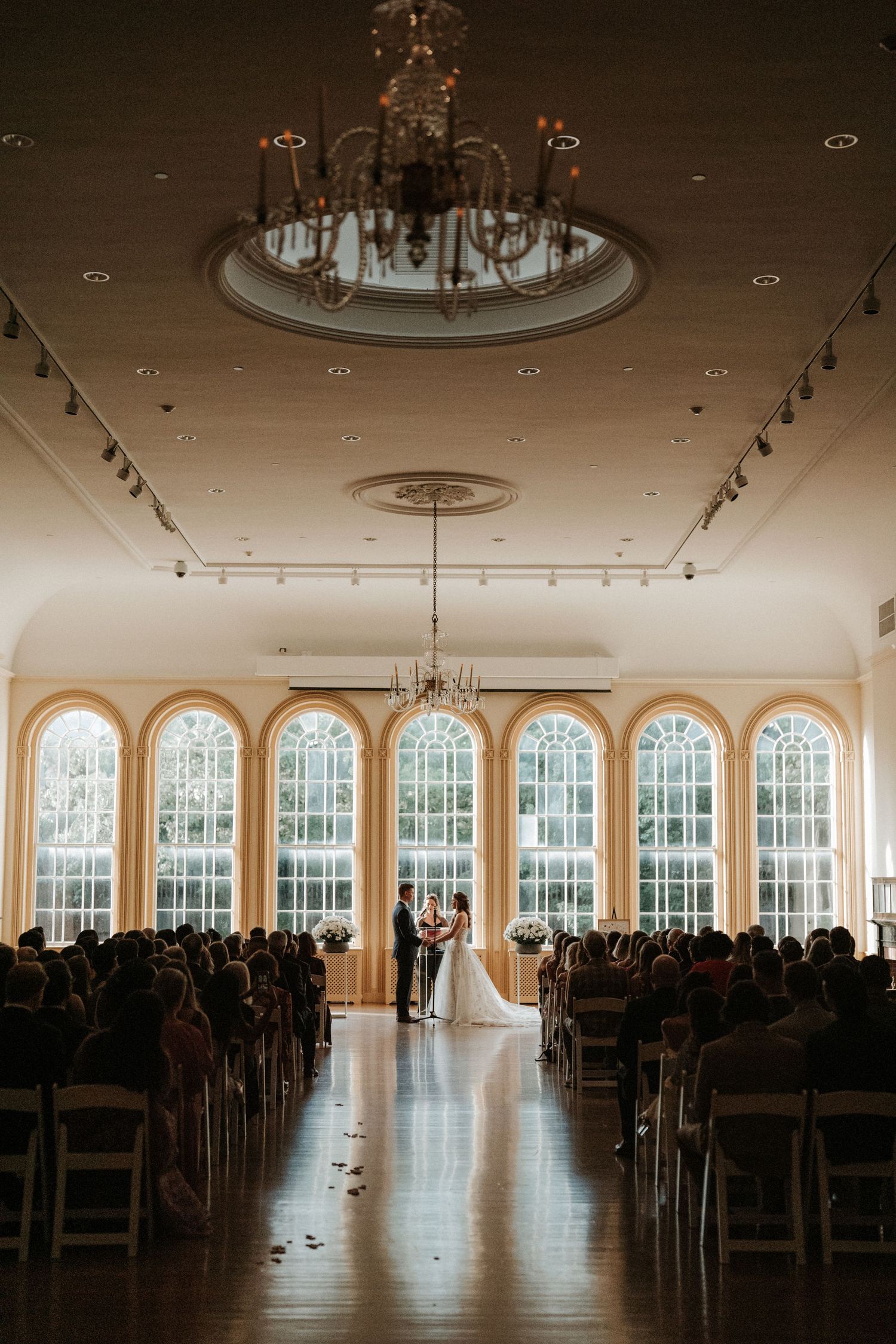 Elegant wedding venue with arched windows and chandelier set up for ceremony.