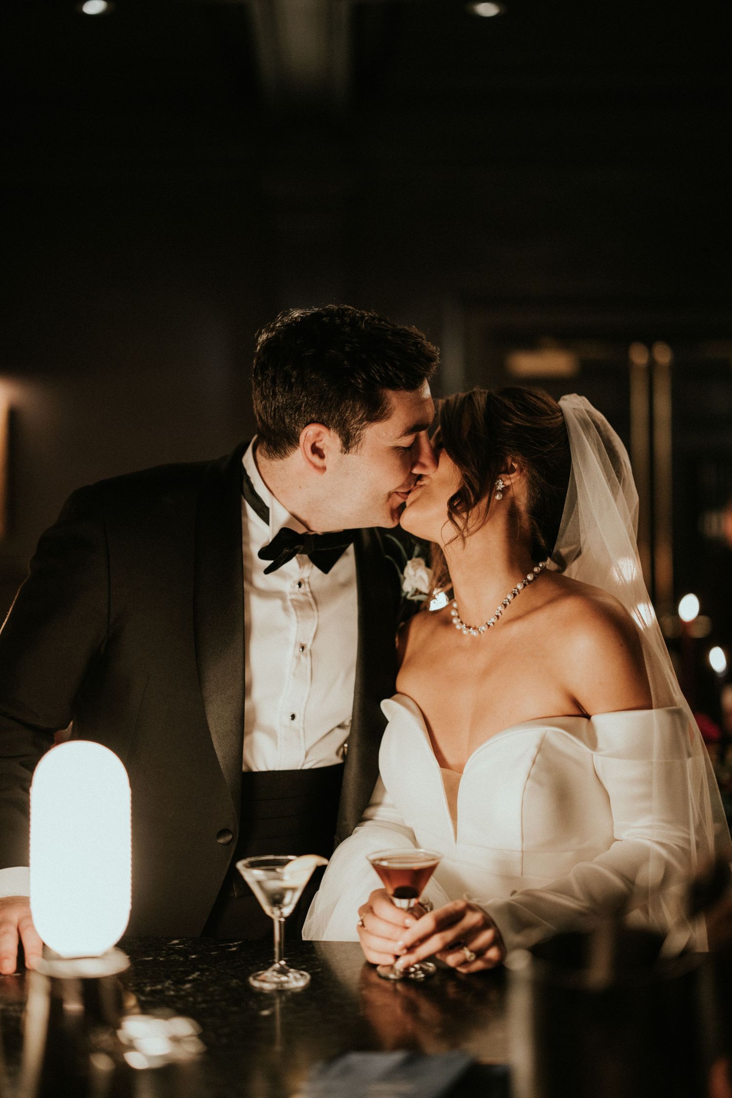 Romantic wedding couple shares intimate moments at candlelit reception in elegant black and white formal attire.