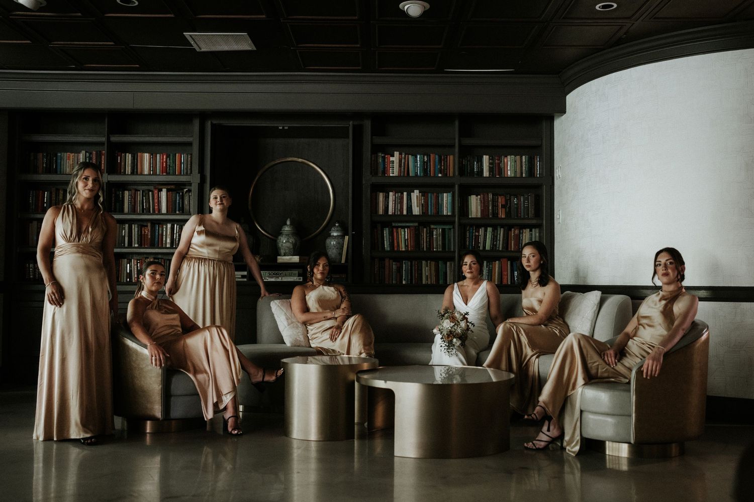 Wedding party seated in a library with bookshelves creating a cozy atmosphere.