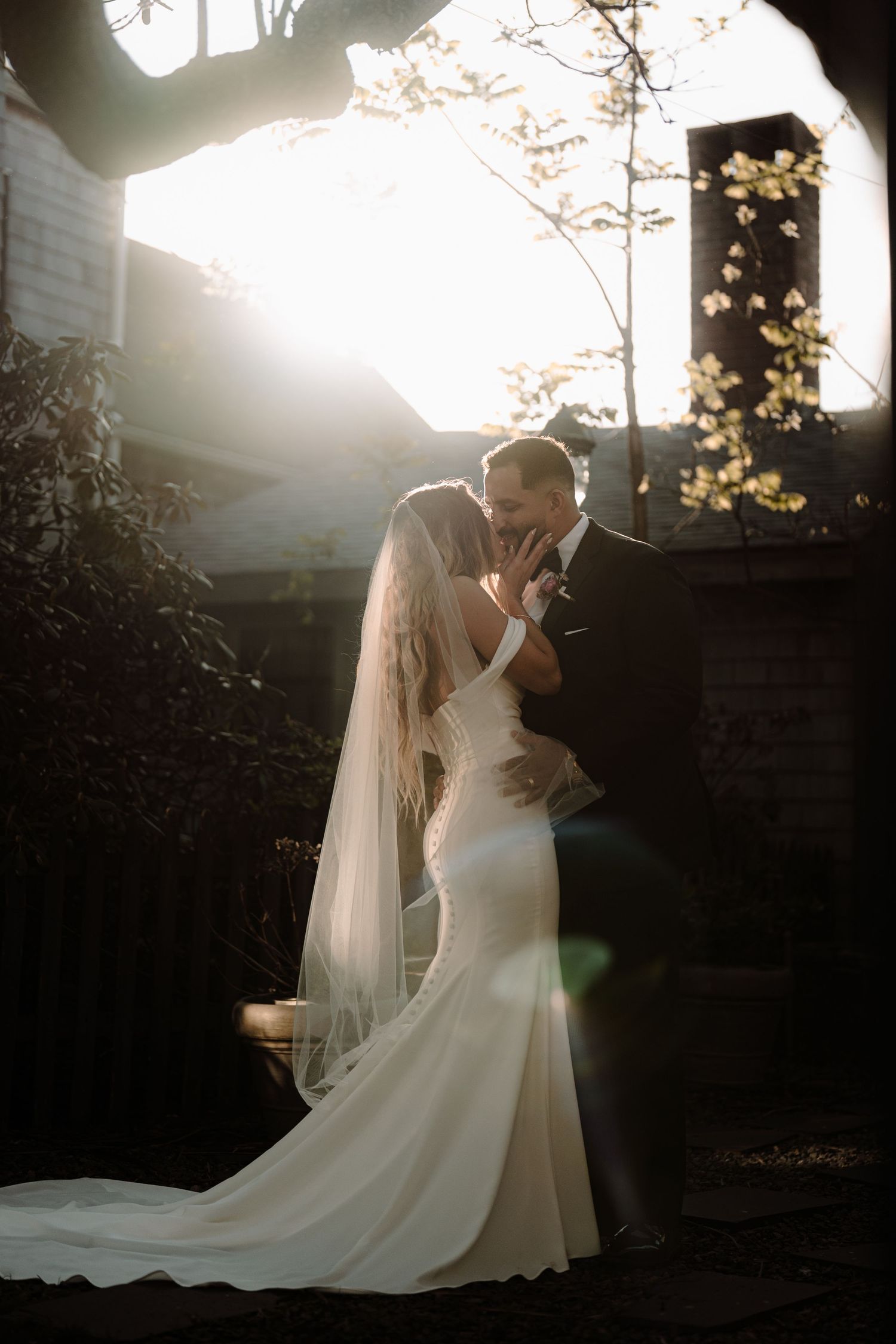 Backlit wedding portrait with sunflare through trees creating dreamy atmosphere.