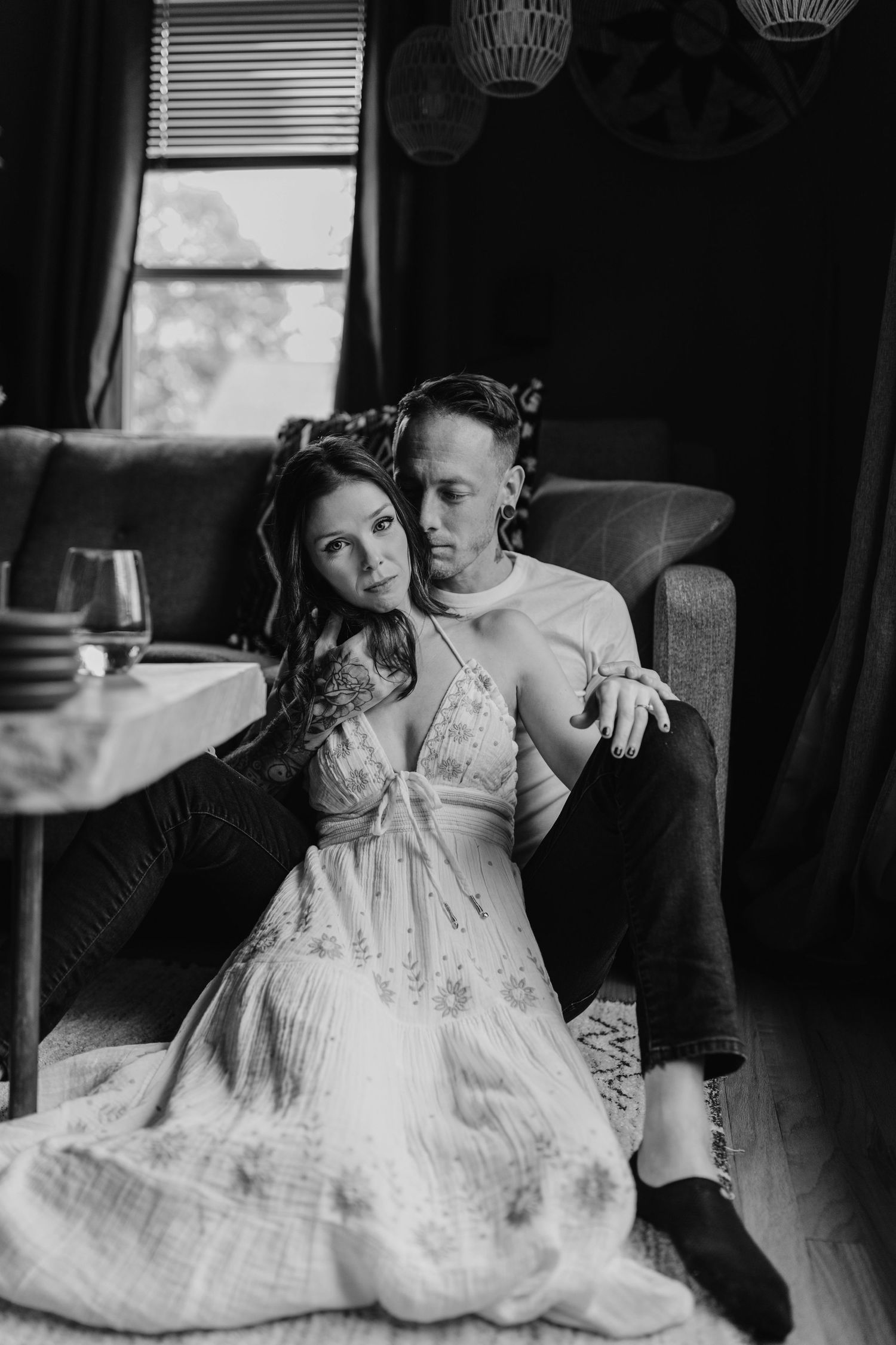 Intimate black and white photo of couple lounging in dimly lit room with window light.