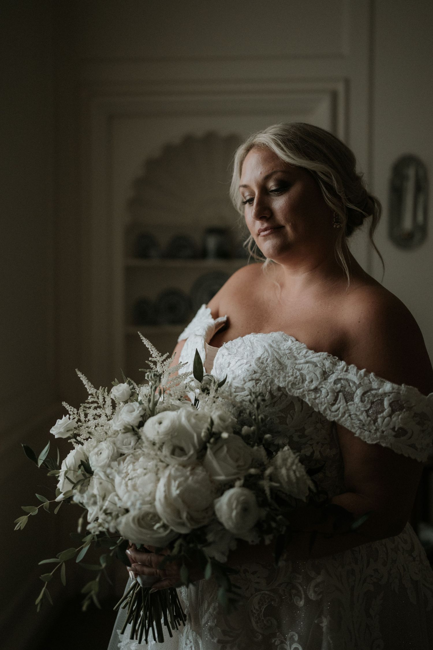 Delicate white wedding bouquet with roses and greenery in moody lighting.