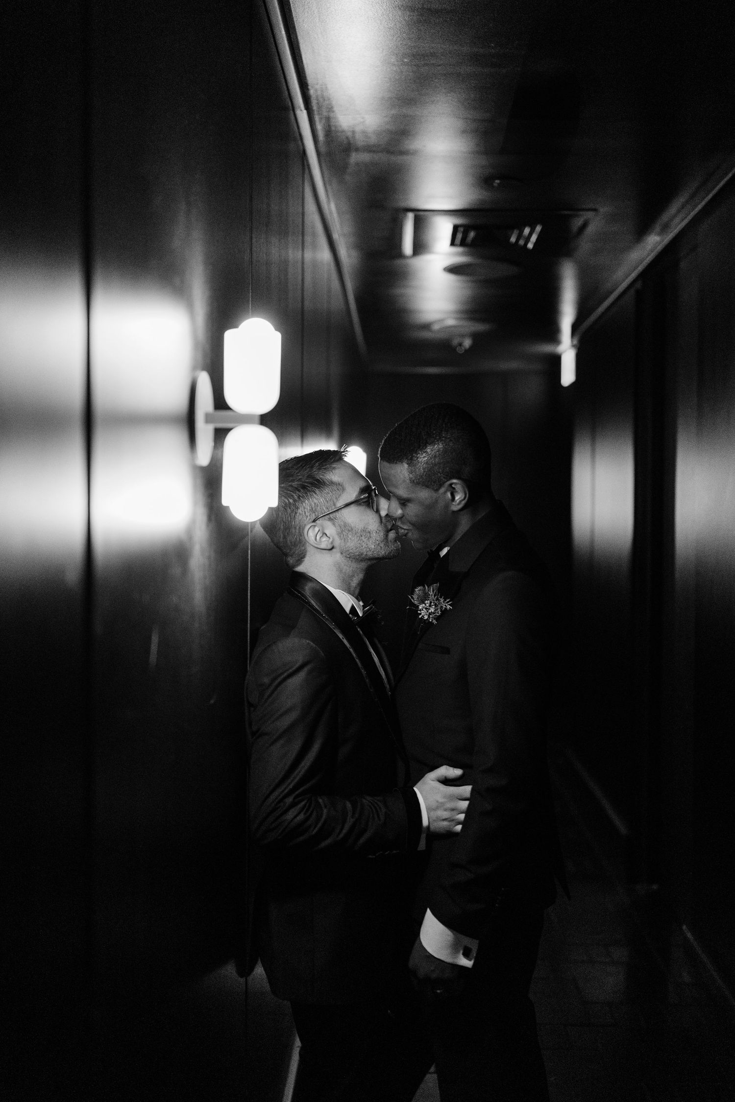 Romantic black and white photo of a couple sharing an intimate moment in a dimly lit hallway.