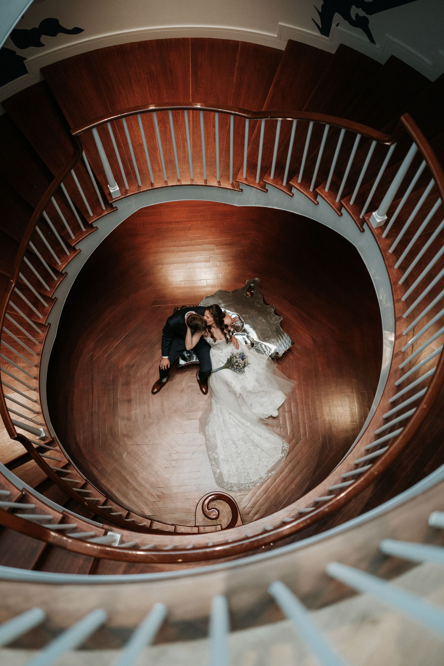 Aerial view of couple dancing on spiral wooden staircase in dramatic lighting.