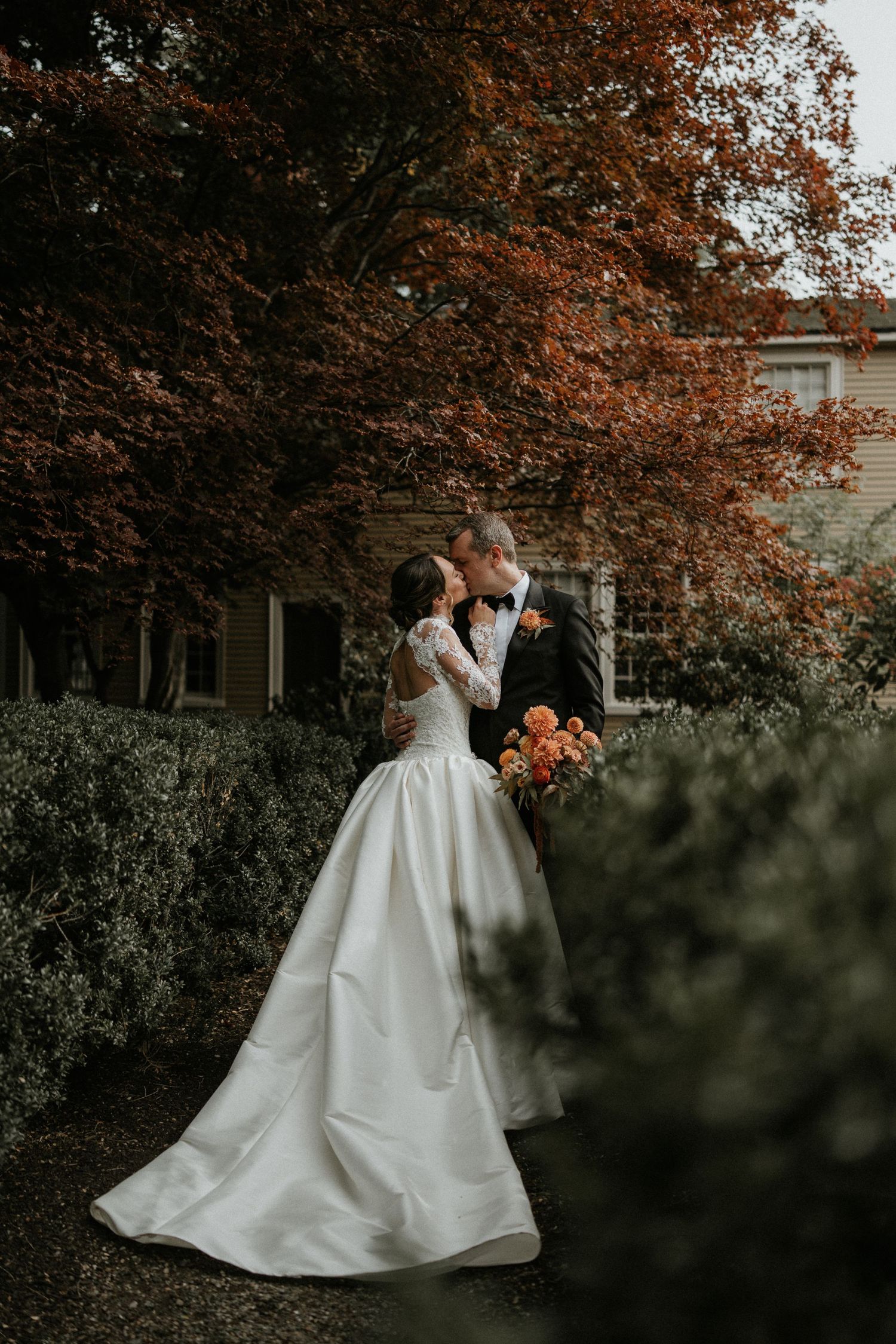 Bride and groom share a romantic kiss in a garden surrounded by autumn foliage, bride wearing a white ball gown.