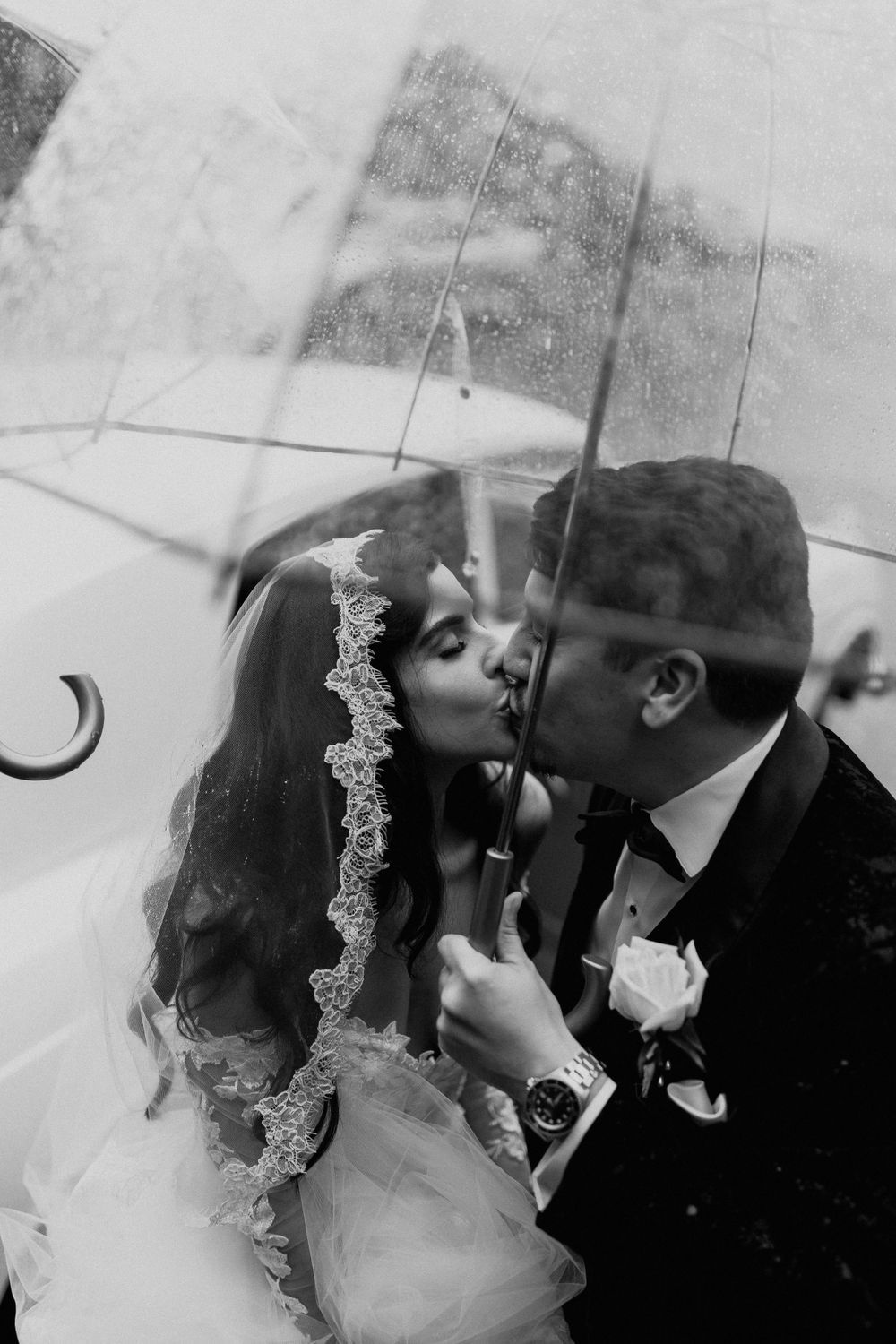 Black and white wedding photo of a couple sharing a kiss under a delicate lace veil.