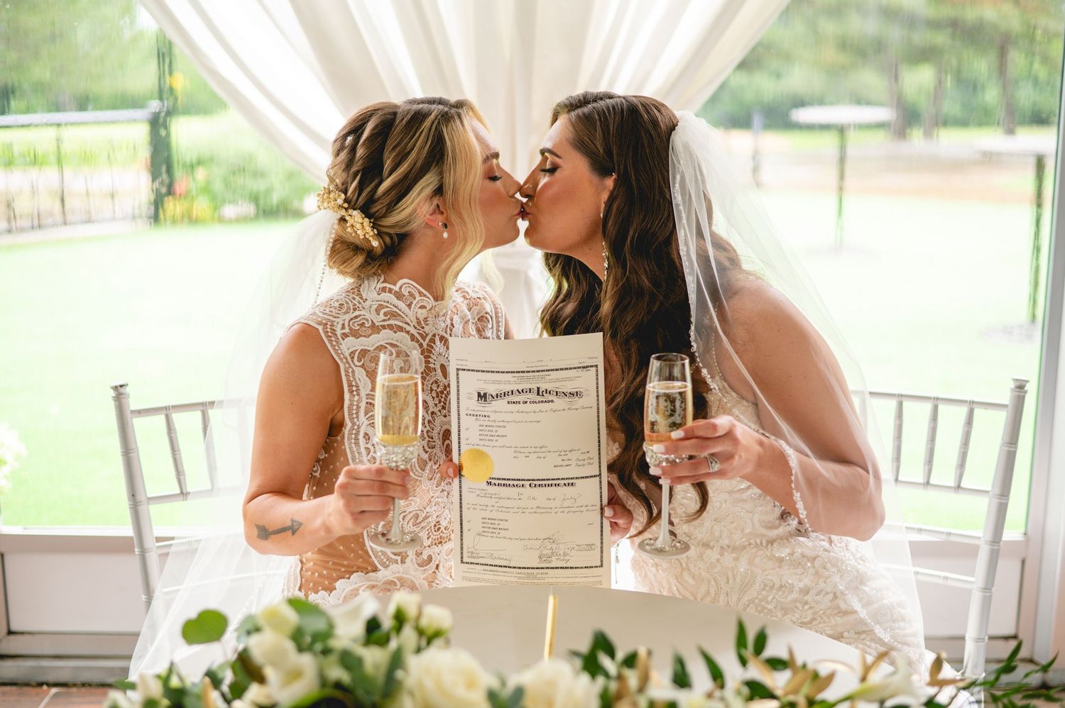 Two people in formal attire share an intimate moment at an elegant wedding reception with white decor and floral details.