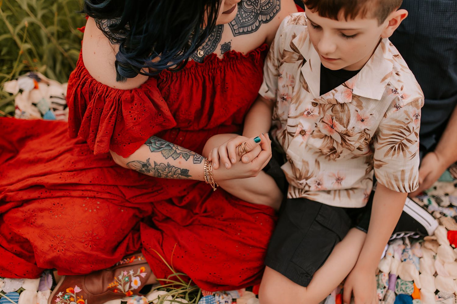 A family sits together on grass in coordinating red and floral outfits during an outdoor photo session.