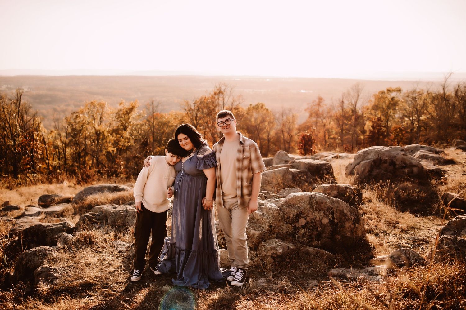 A family stands together on a rocky overlook during golden hour with autumn trees in the background.