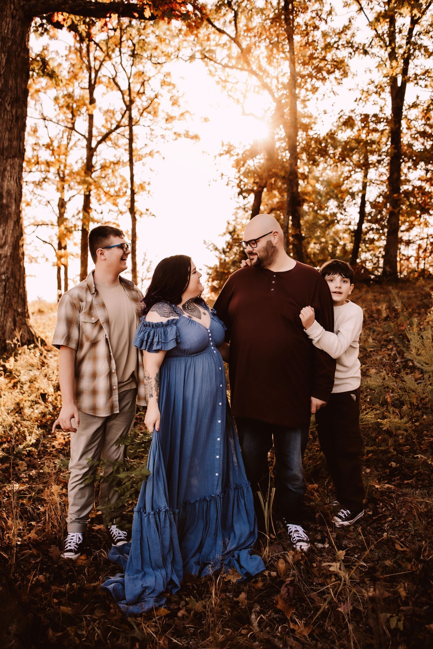 A family poses together in a forest setting during golden hour sunset with warm autumn lighting and fallen leaves.